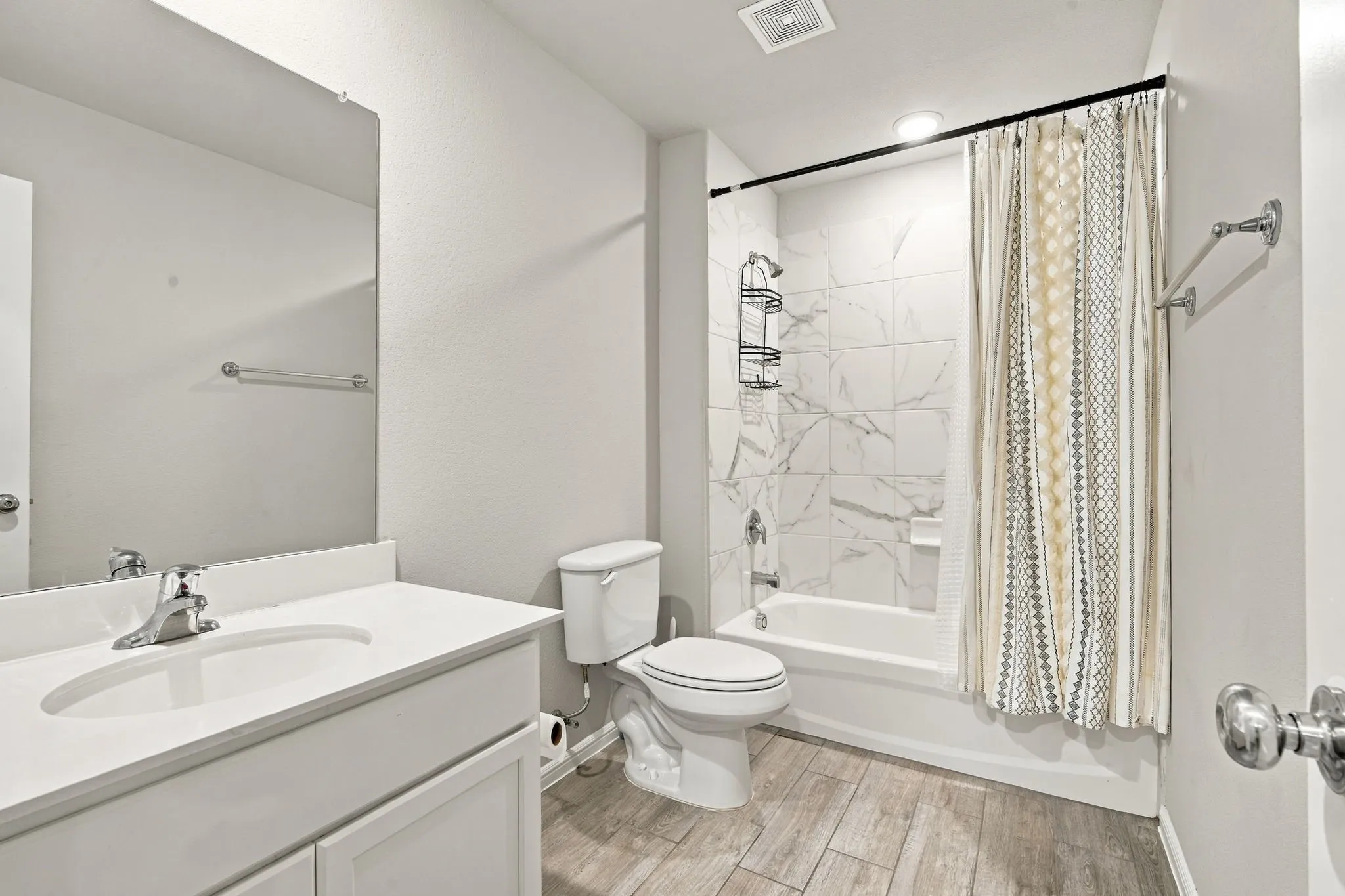 Bathroom featuring a single vanity with an integrated sink, wood-finish flooring, a toilet, and a shower-tub combination with tiled walls