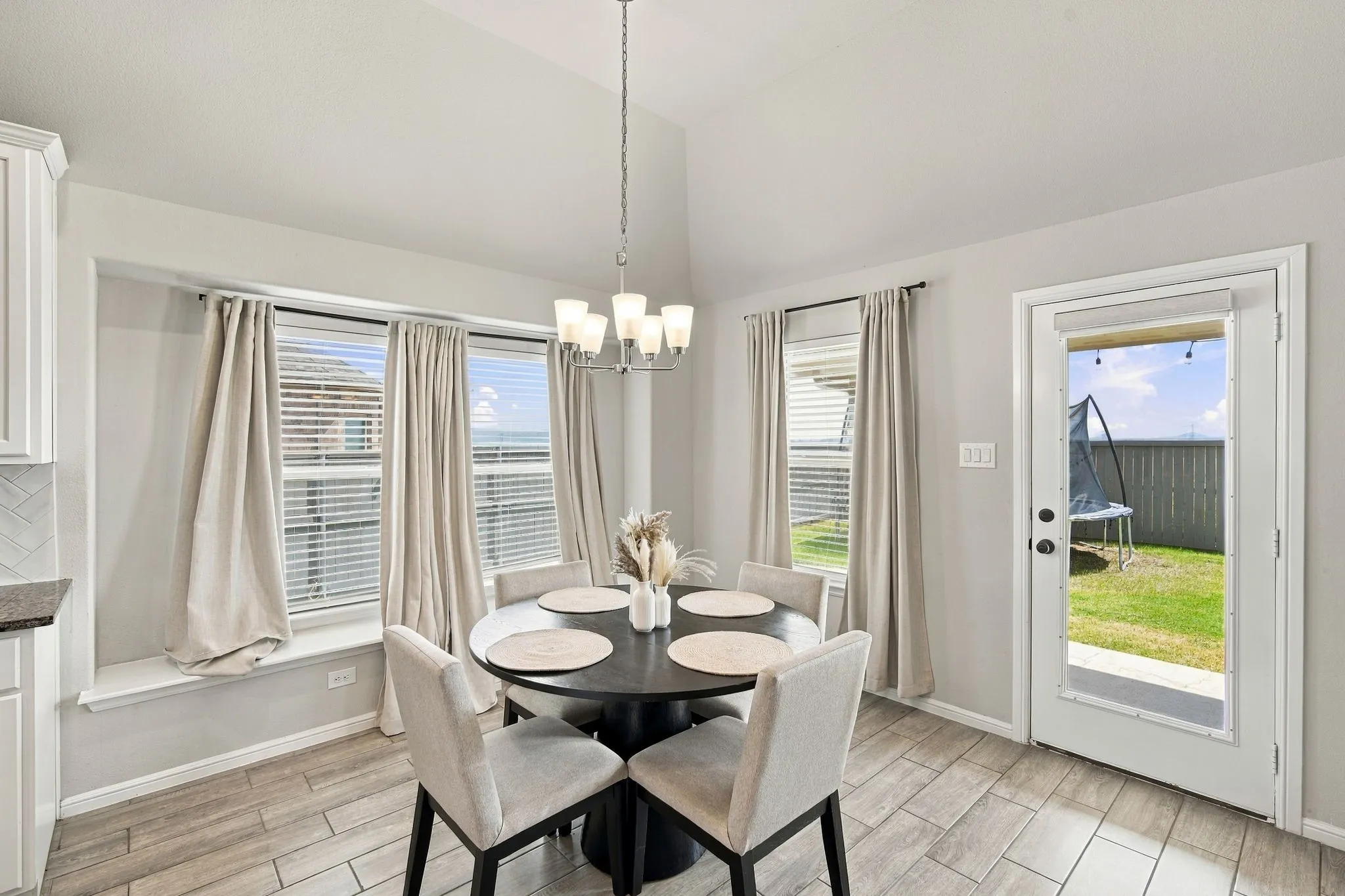 Vaulted ceiling with chandelier, tiled flooring, built-in window bench, multiple windows, and a glass-paneled exterior door