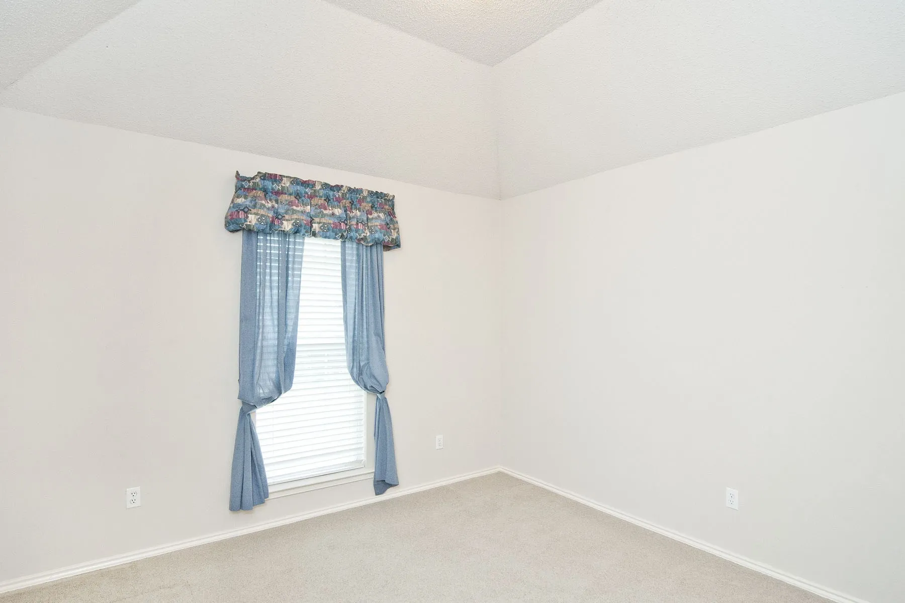 Empty room featuring light carpet, baseboards, and vaulted ceiling