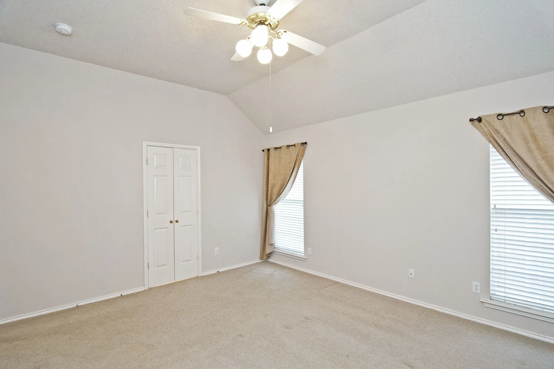 Spare room featuring vaulted ceiling, baseboards, light colored carpet, and ceiling fan
