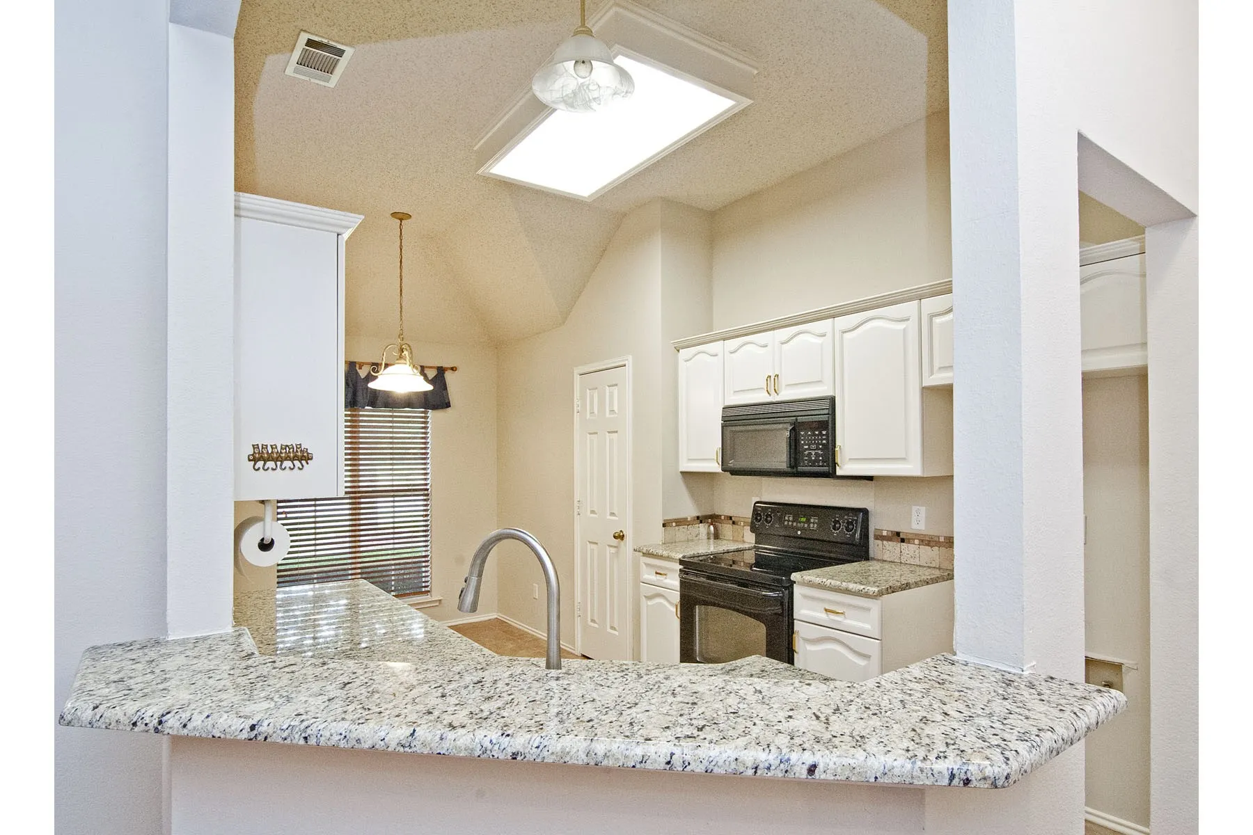 Kitchen with a sink, vaulted ceiling with skylight, visible vents, light stone countertops, and black appliances
