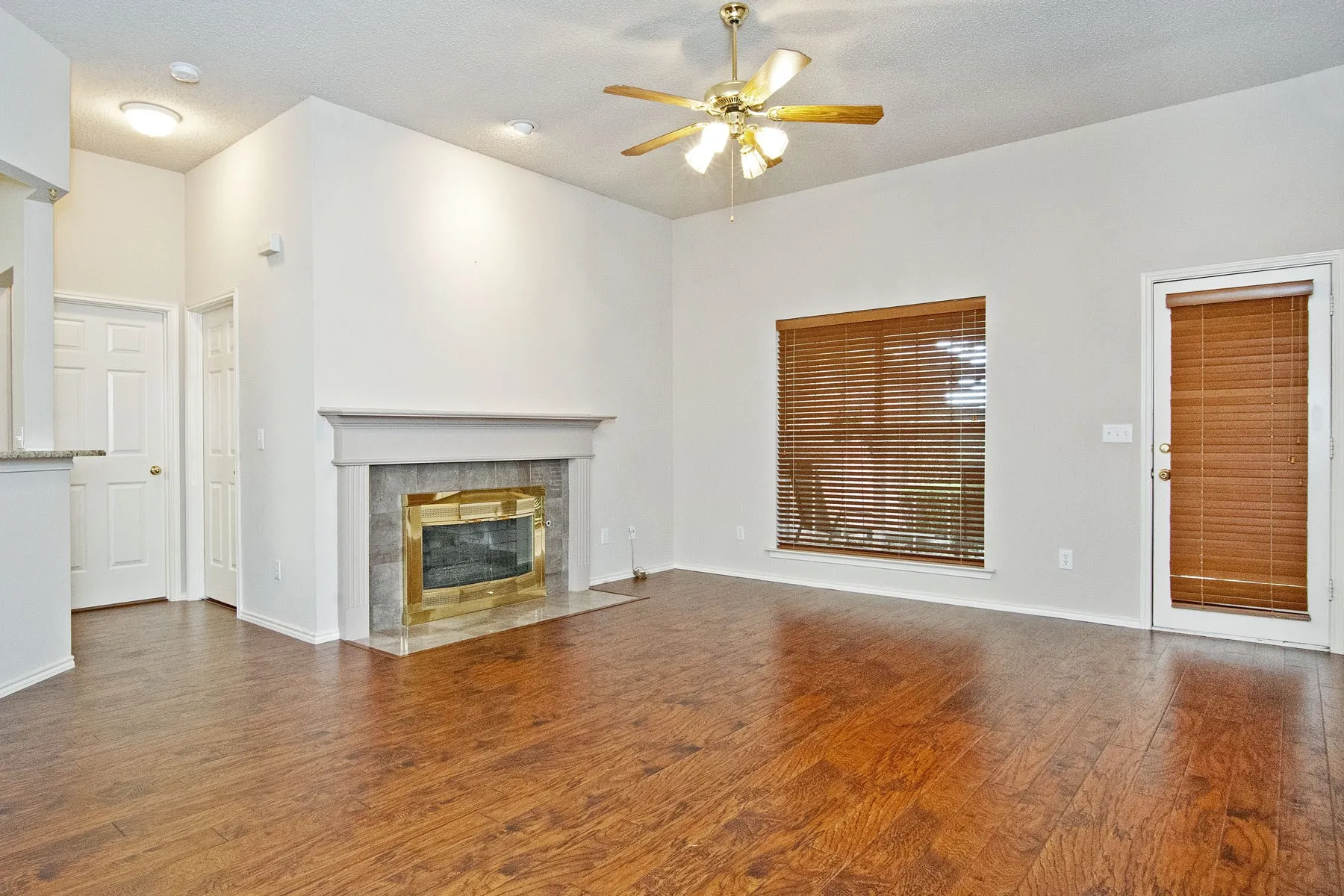 Unfurnished living room with wood-type flooring, baseboards, a textured ceiling, ceiling fan, and a tiled fireplace