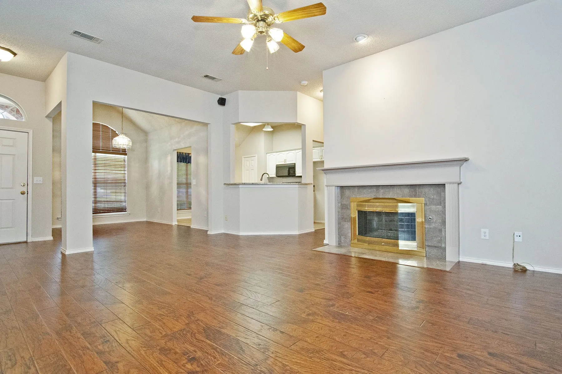 Unfurnished living room featuring hardwood / wood-style floors, baseboards, visible vents, and a ceiling fan