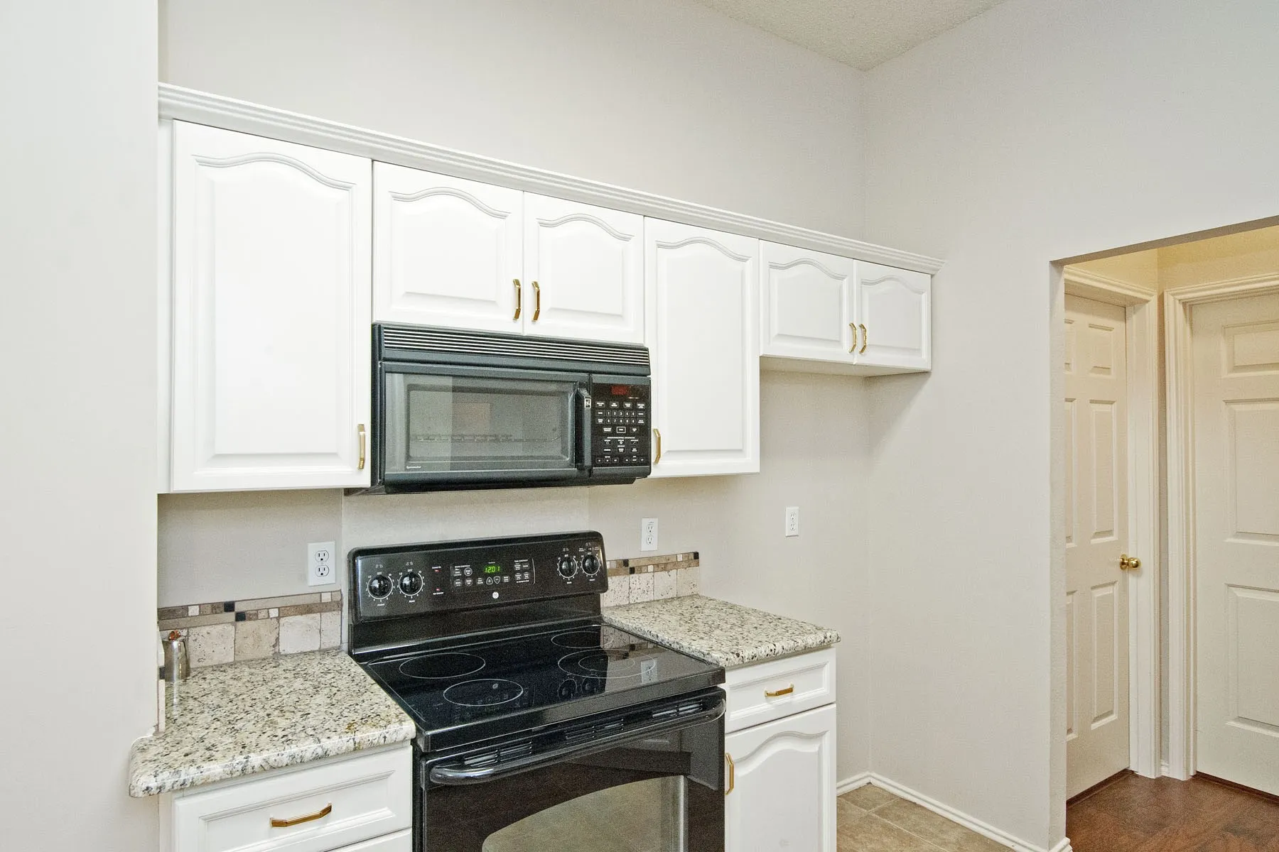 Kitchen featuring white cabinets, light stone countertops, baseboards, and black appliances