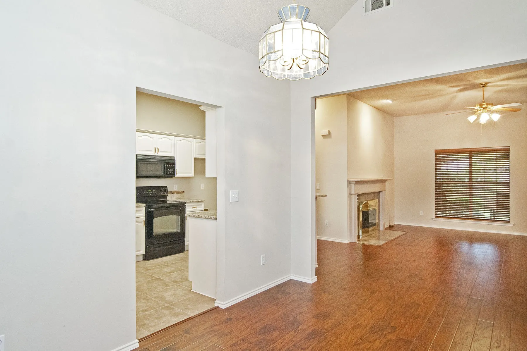 Unfurnished living room with visible vents, a high end fireplace, light wood finished floors, baseboards, and ceiling fan with notable chandelier