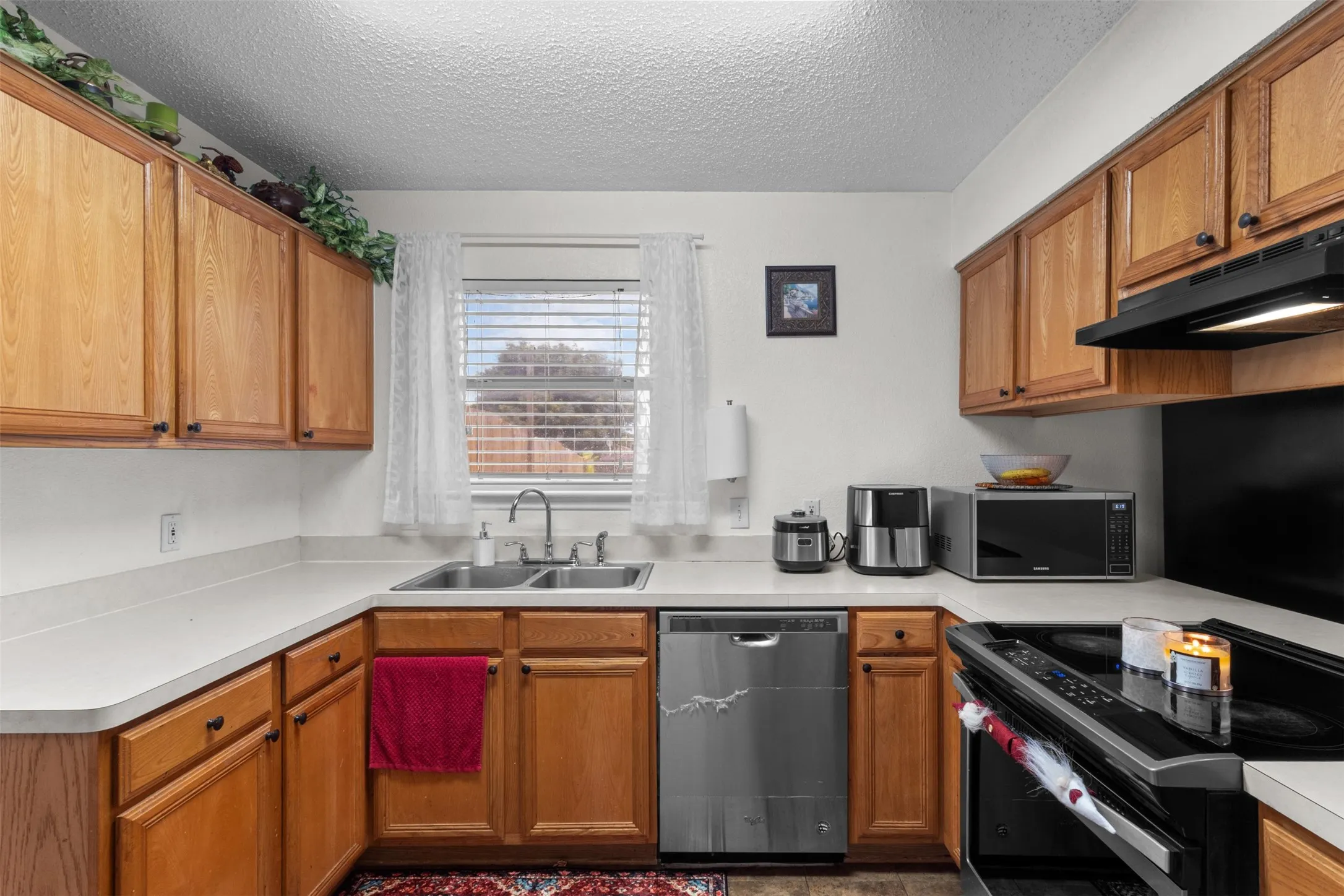 Functional kitchen featuring a double basin sink, stainless steel dishwasher, matching range hood, and ample cabinetry