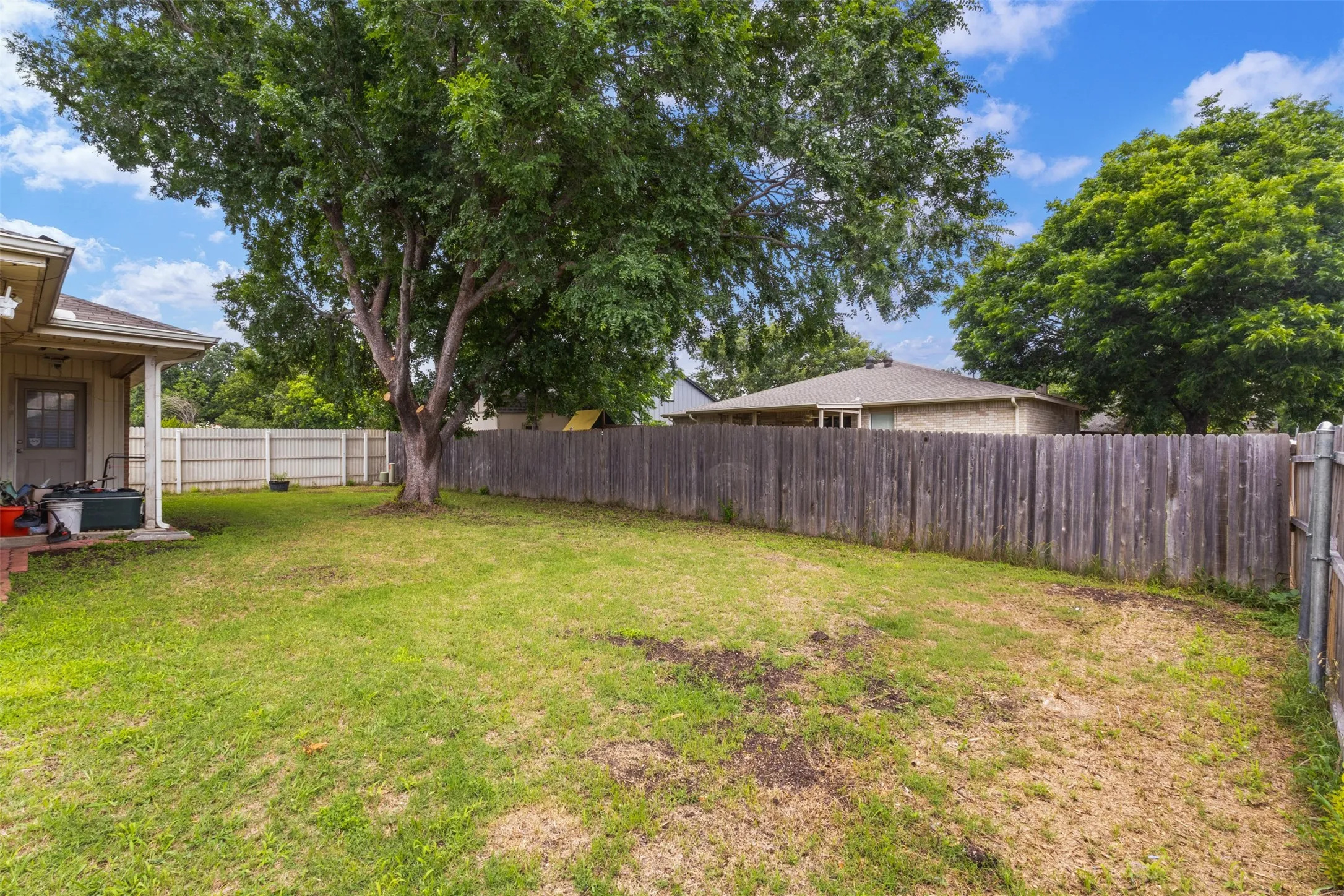Expansive backyard featuring mature trees and a wooden privacy fence