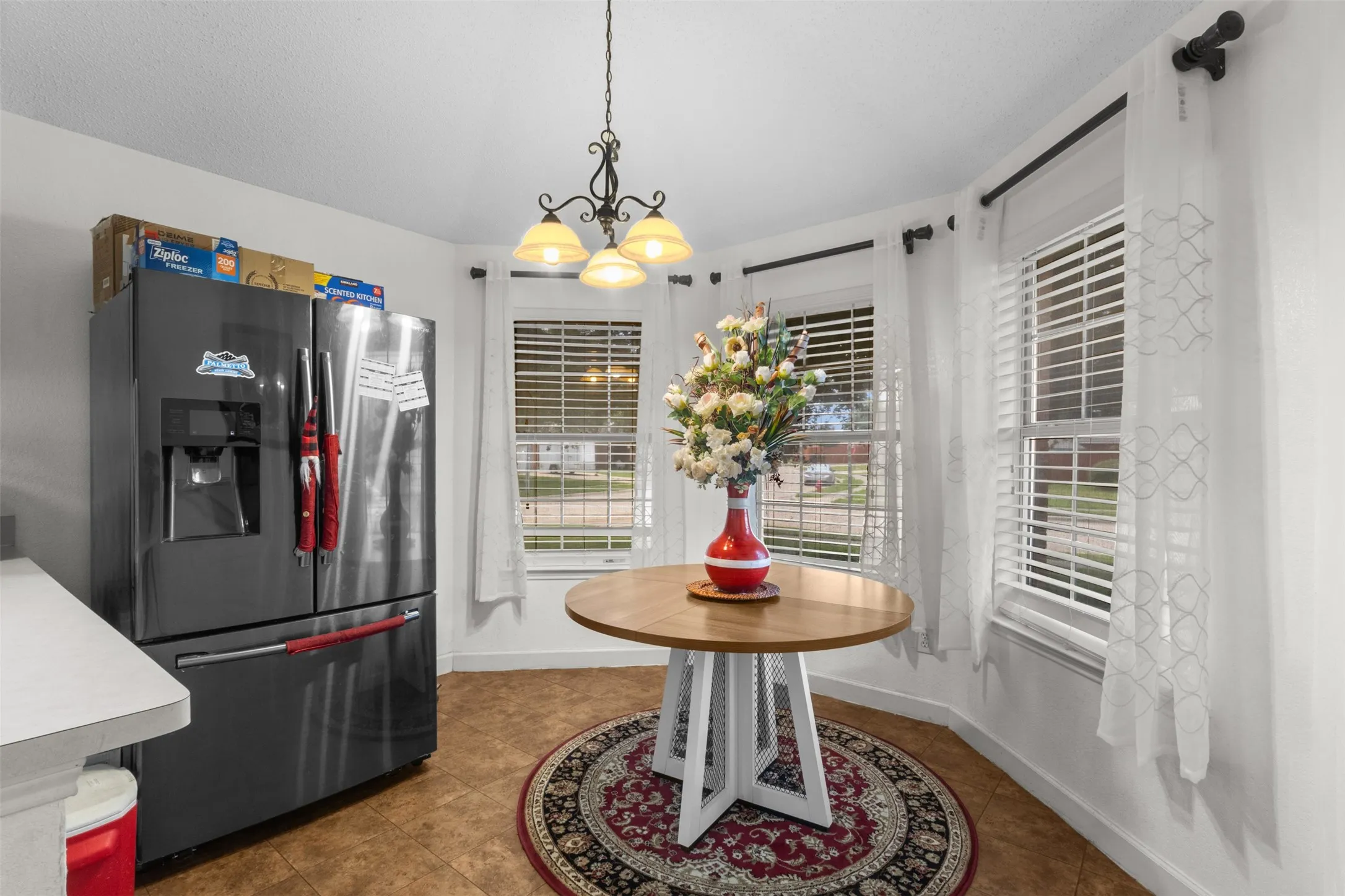 Bay window with horizontal blinds, ceiling-mounted chandelier, and tile flooring