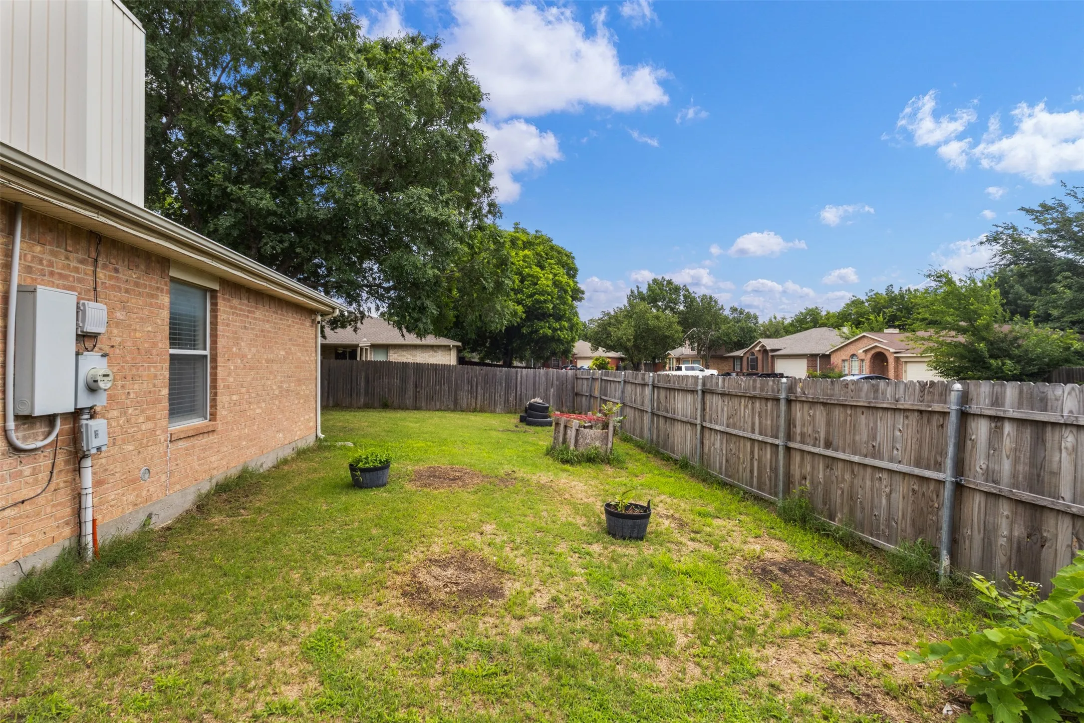 Expansive backyard featuring a wood privacy fence, a brick exterior, and mature trees