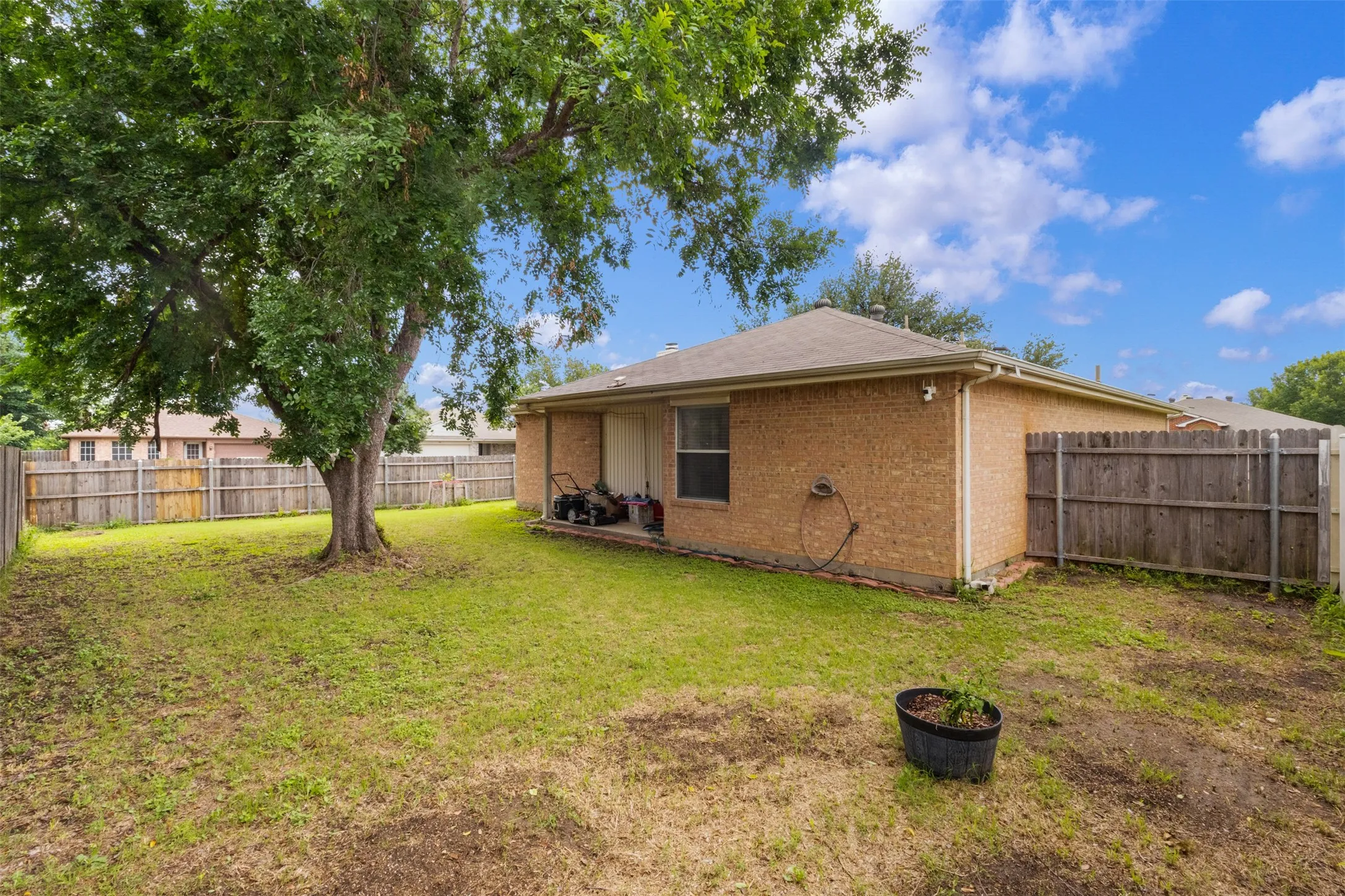 Expansive backyard featuring a mature shade tree, privacy fencing, and a brick exterior