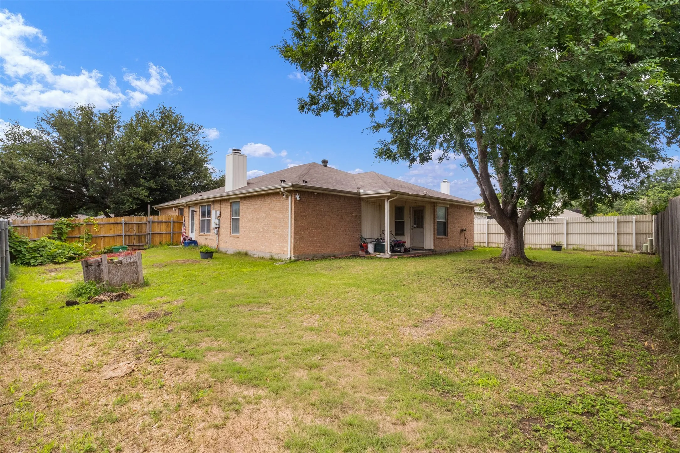 Expansive backyard featuring a mature tree, privacy fencing, brick exterior, and covered patio