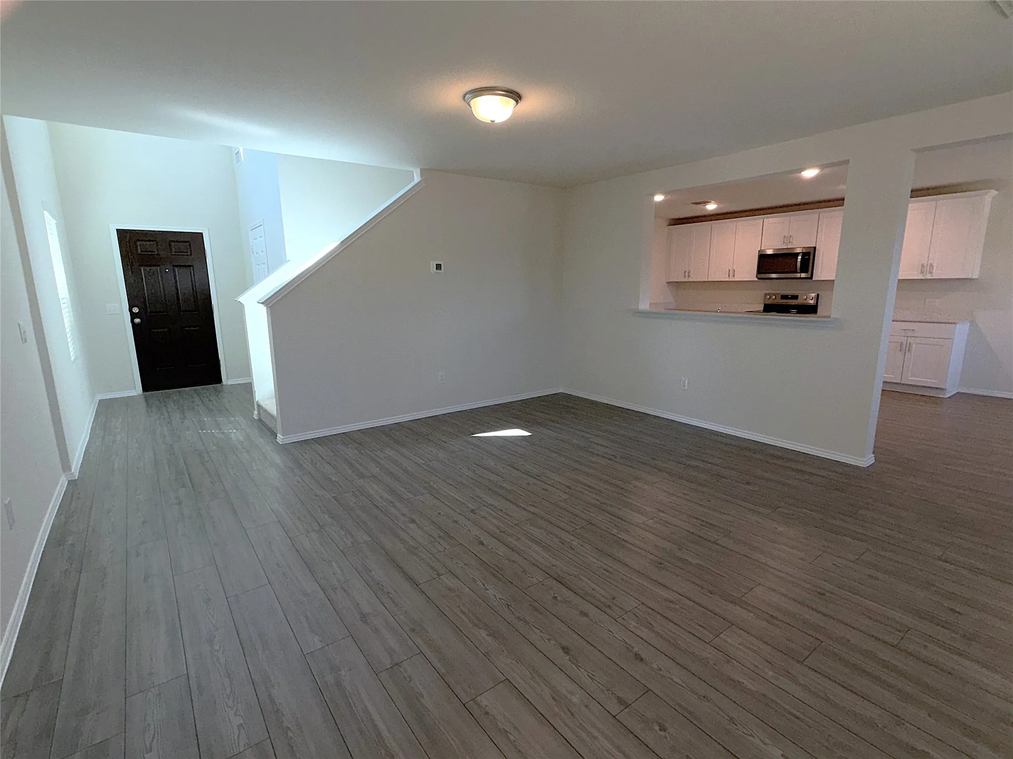 Vinyl plank flooring throughout, kitchen with white cabinetry and built-in appliances, recessed lighting, and a dark paneled entry door