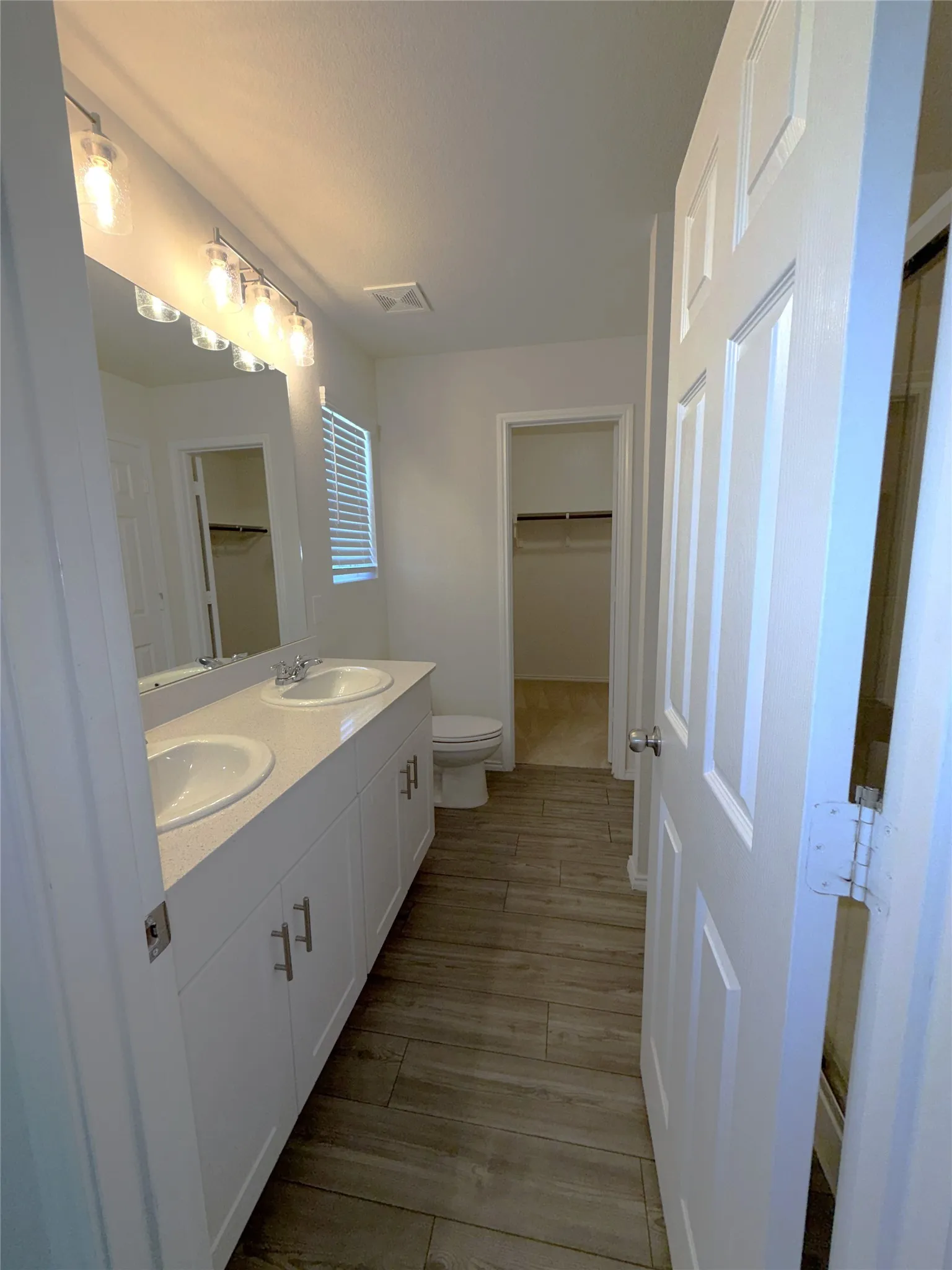 Dual vanity with white cabinetry, wood-finish flooring, and a walk-in shower