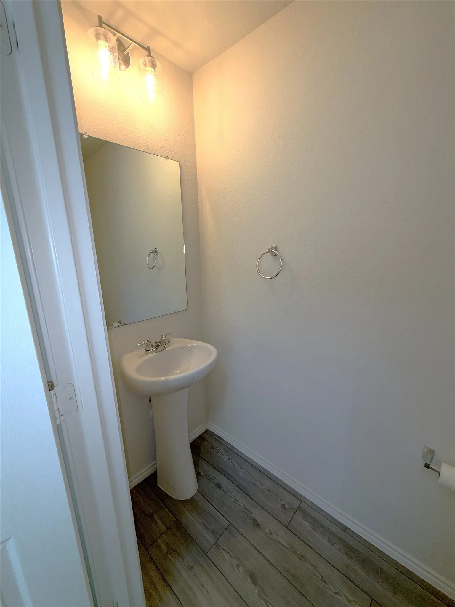 Half bath near entry with Pedestal sink with chrome fixtures, wall-mounted mirror, and luxury vinyl plank flooring.