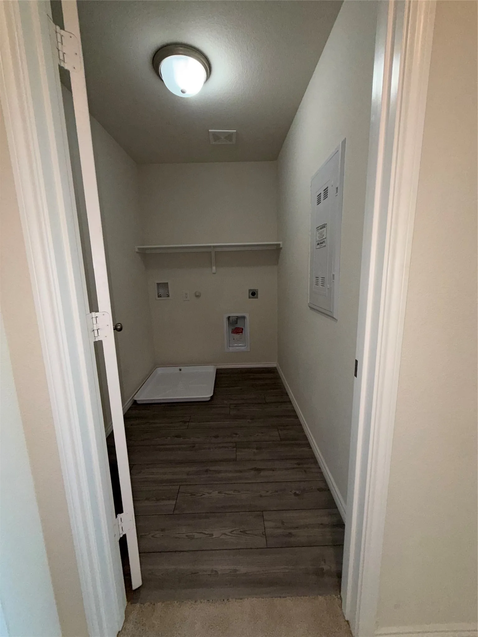 Utility area featuring a wall-mounted shelf, and overhead lighting and drip pan for washing machine.