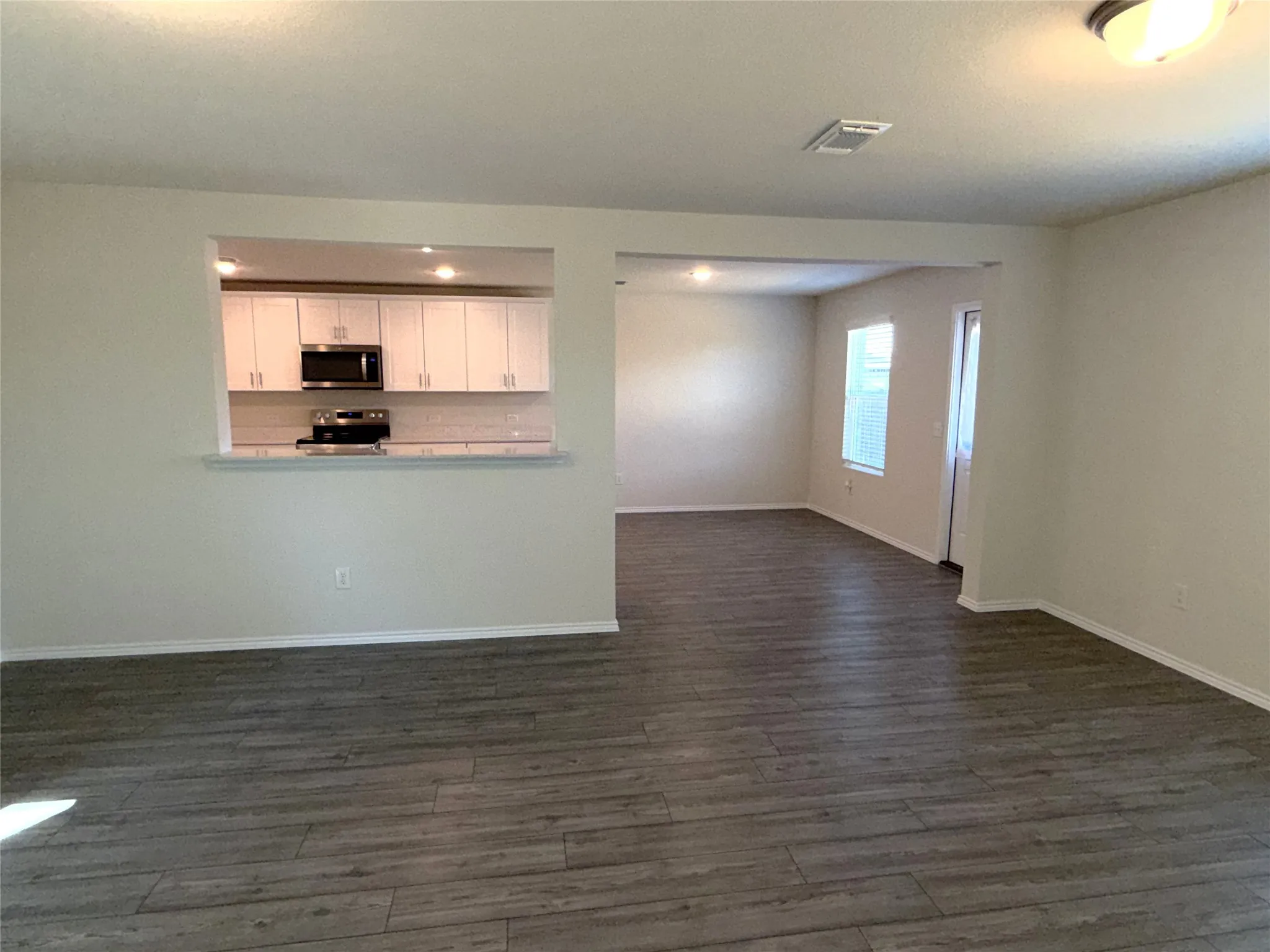 Open concept living space featuring luxury vinyl plank flooring, a kitchen pass-through, recessed lighting, white cabinetry, and stainless steel appliances