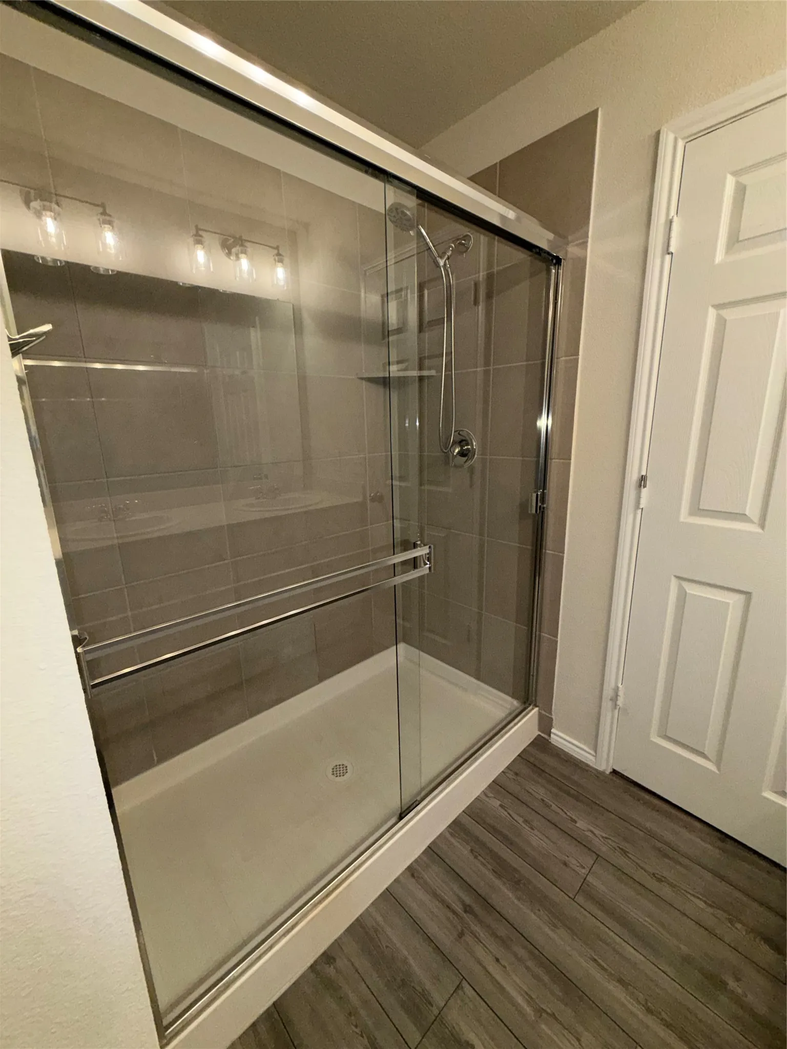 Frameless glass shower enclosure with sliding door, featuring a built-in shower niche and a handheld showerhead