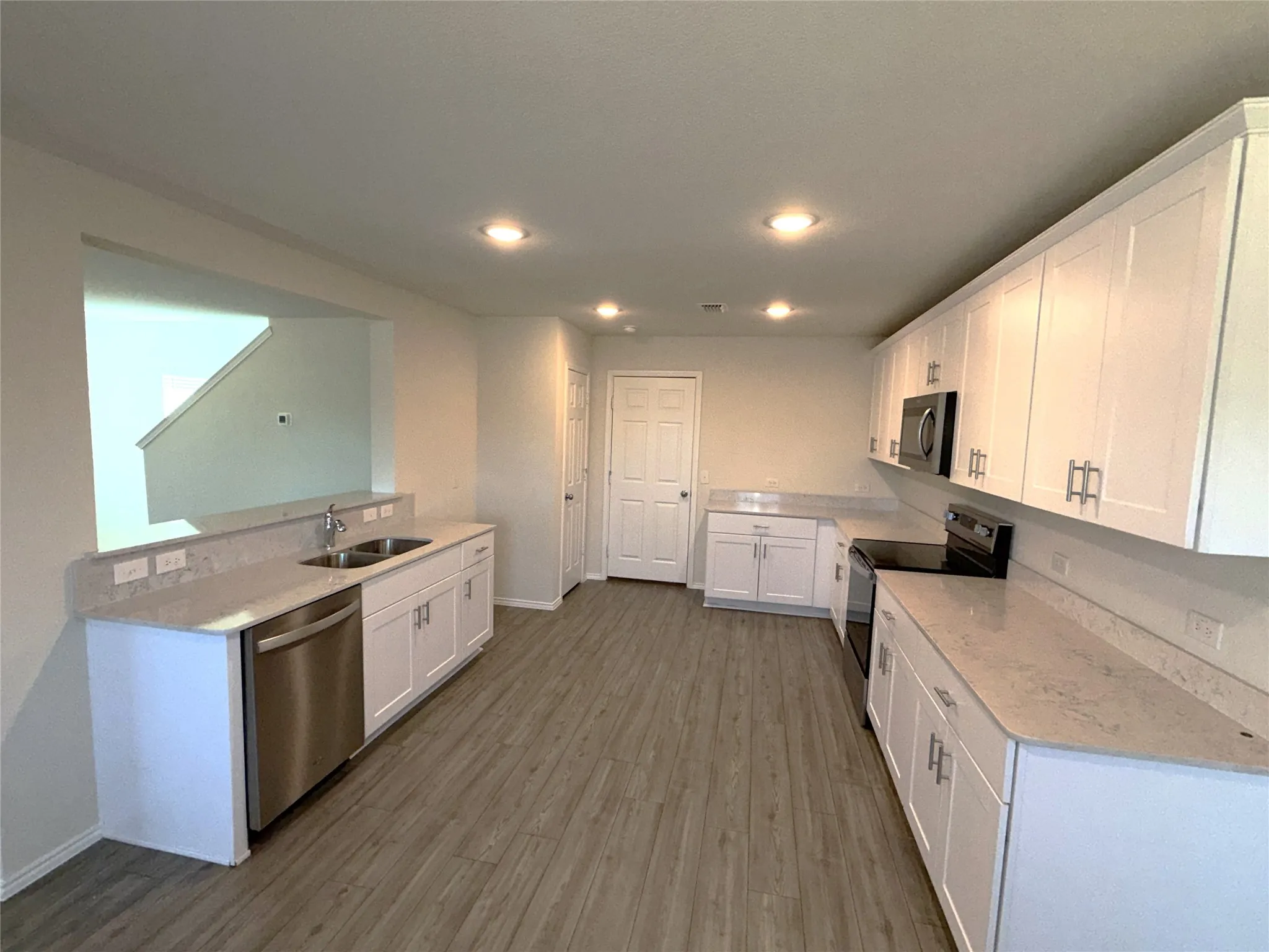 Kitchen featuring white cabinetry, light-toned countertops, stainless steel sink, stainless steel dishwasher, and wood-finish flooring
