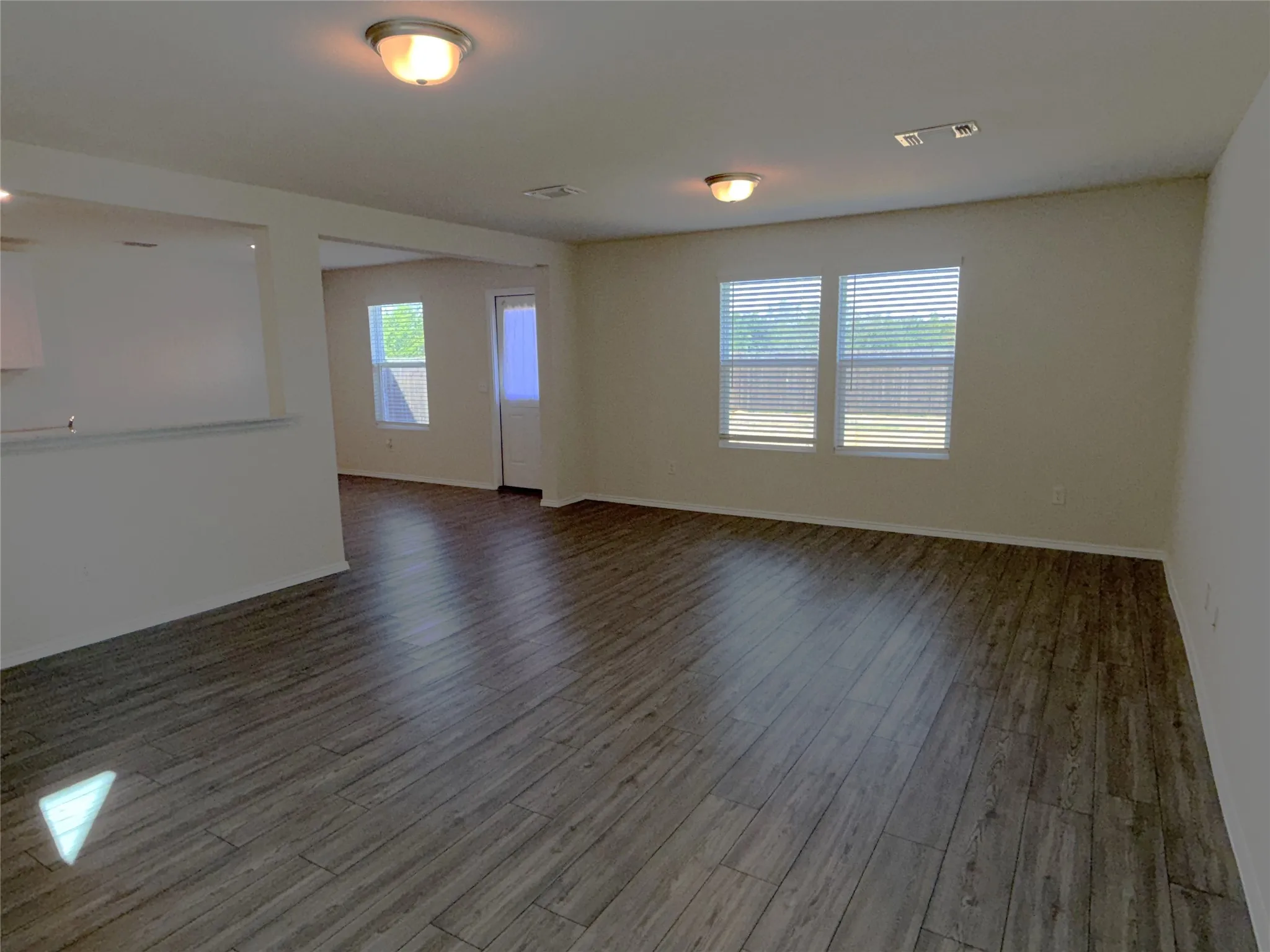 Spacious living room featuring luxury plank flooring, multiple windows with blinds, and flush-mount lighting
