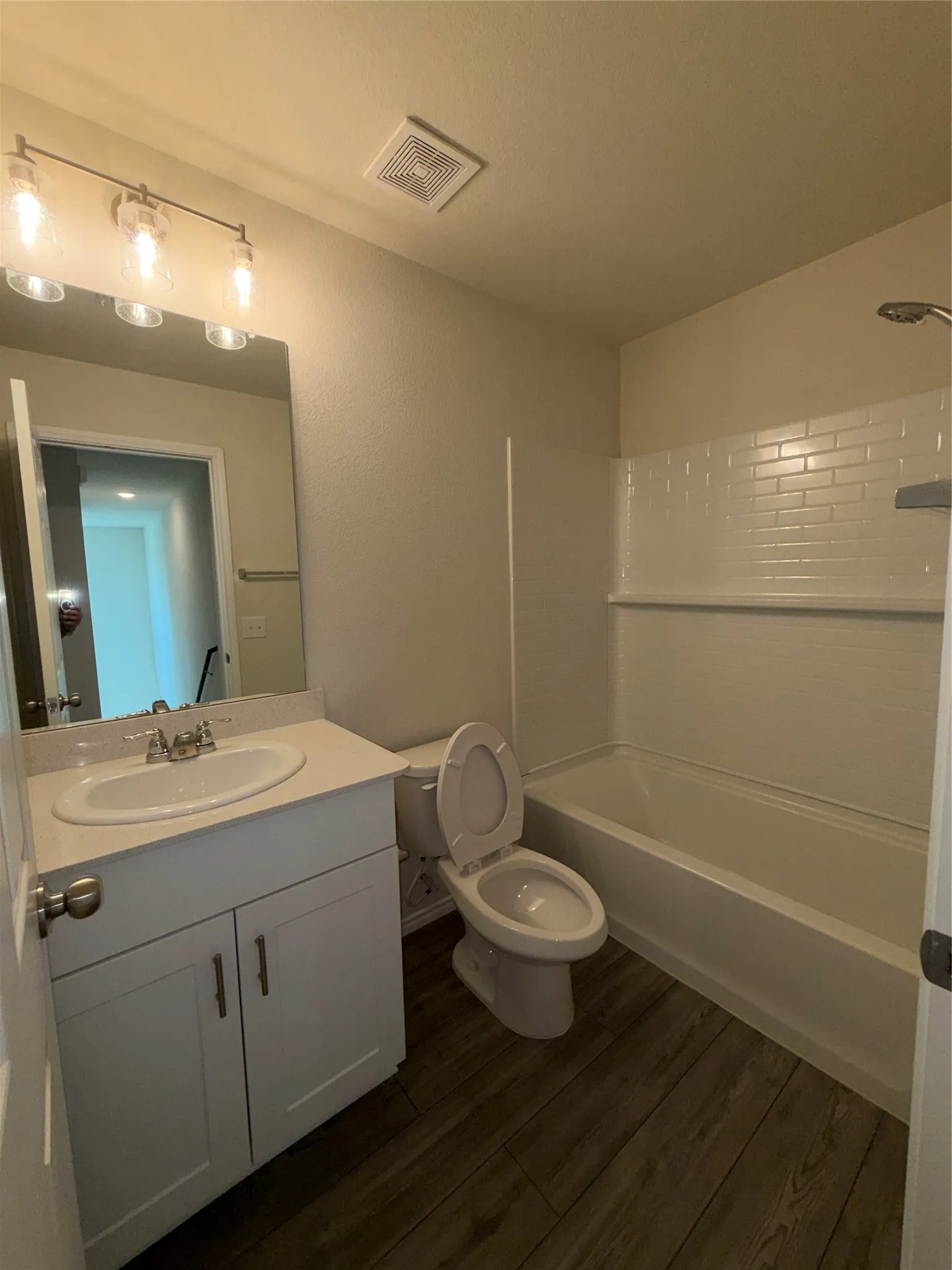 Bathroom featuring a single vanity with stone-finish countertop, vinyl plank flooring, and a bathtub with subway tile type surround