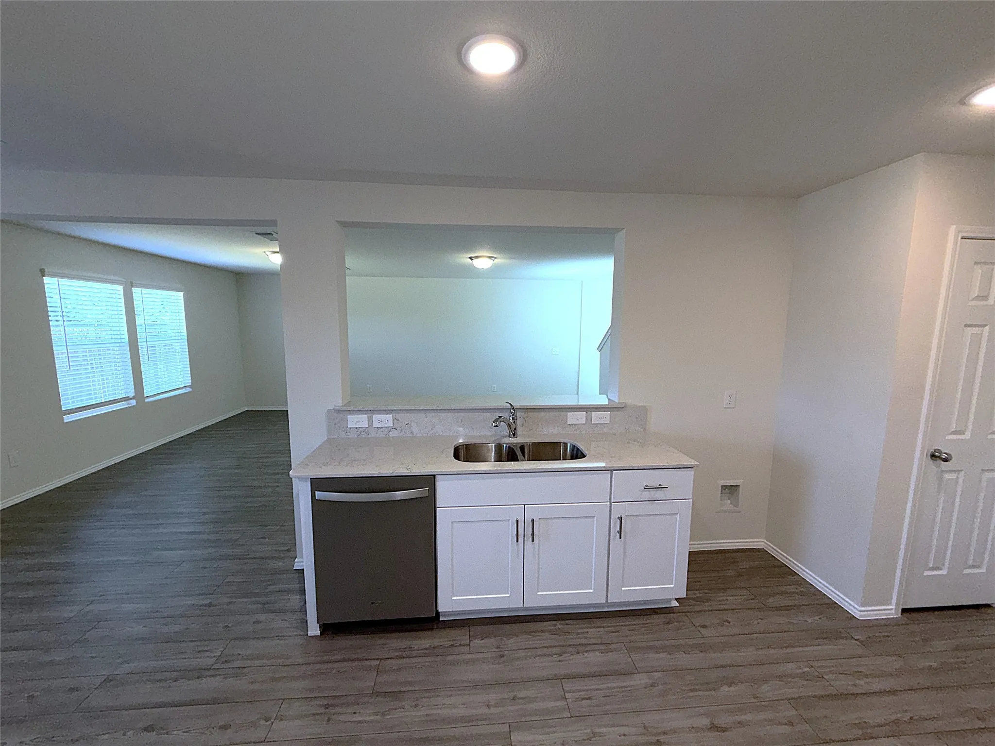 Kitchenette with white cabinetry, stainless steel double basin sink, light-colored stone countertop, and integrated dishwasher