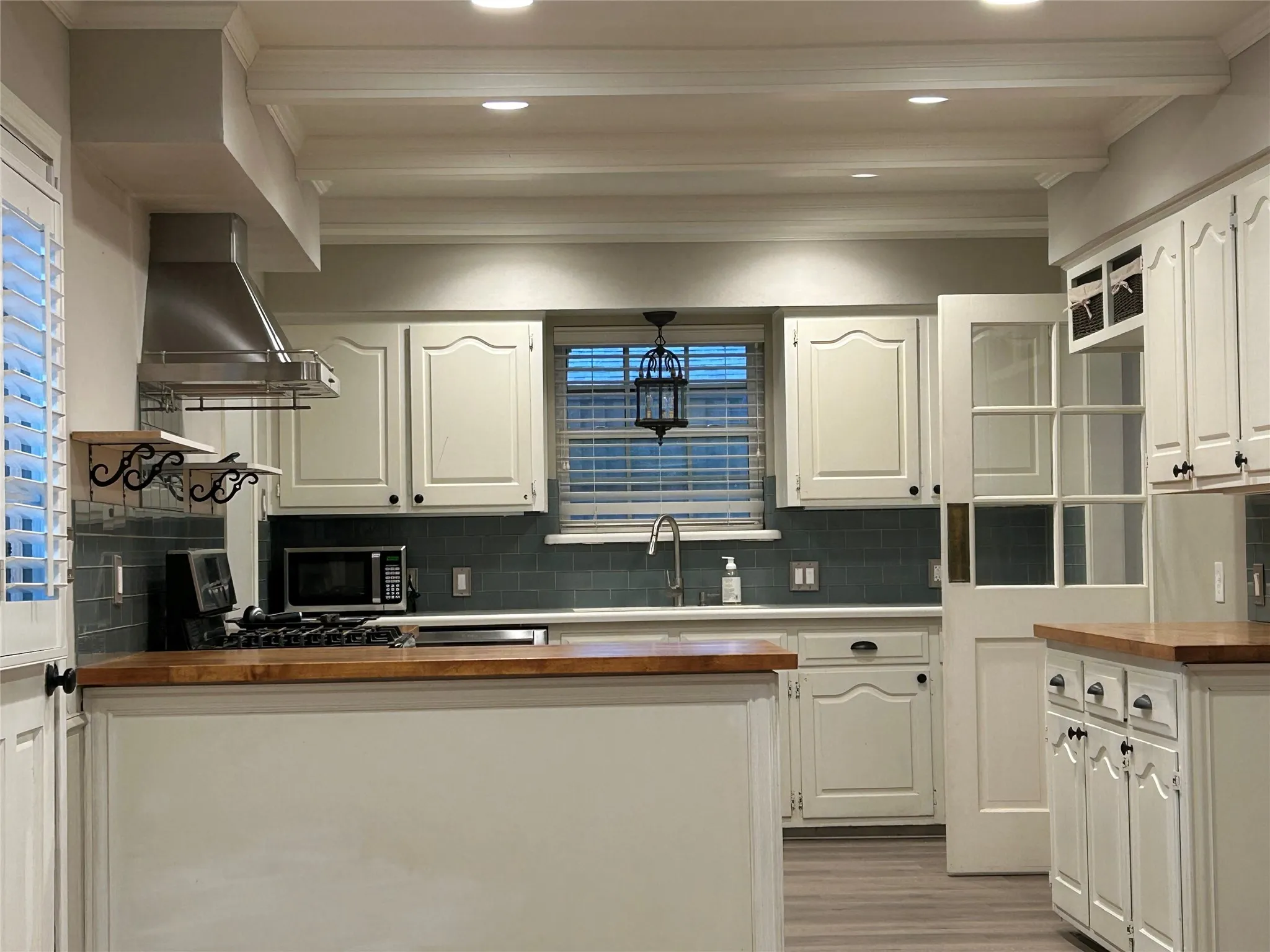 The kitchen has white cabinetry, recessed lighting, and ceiling beams.