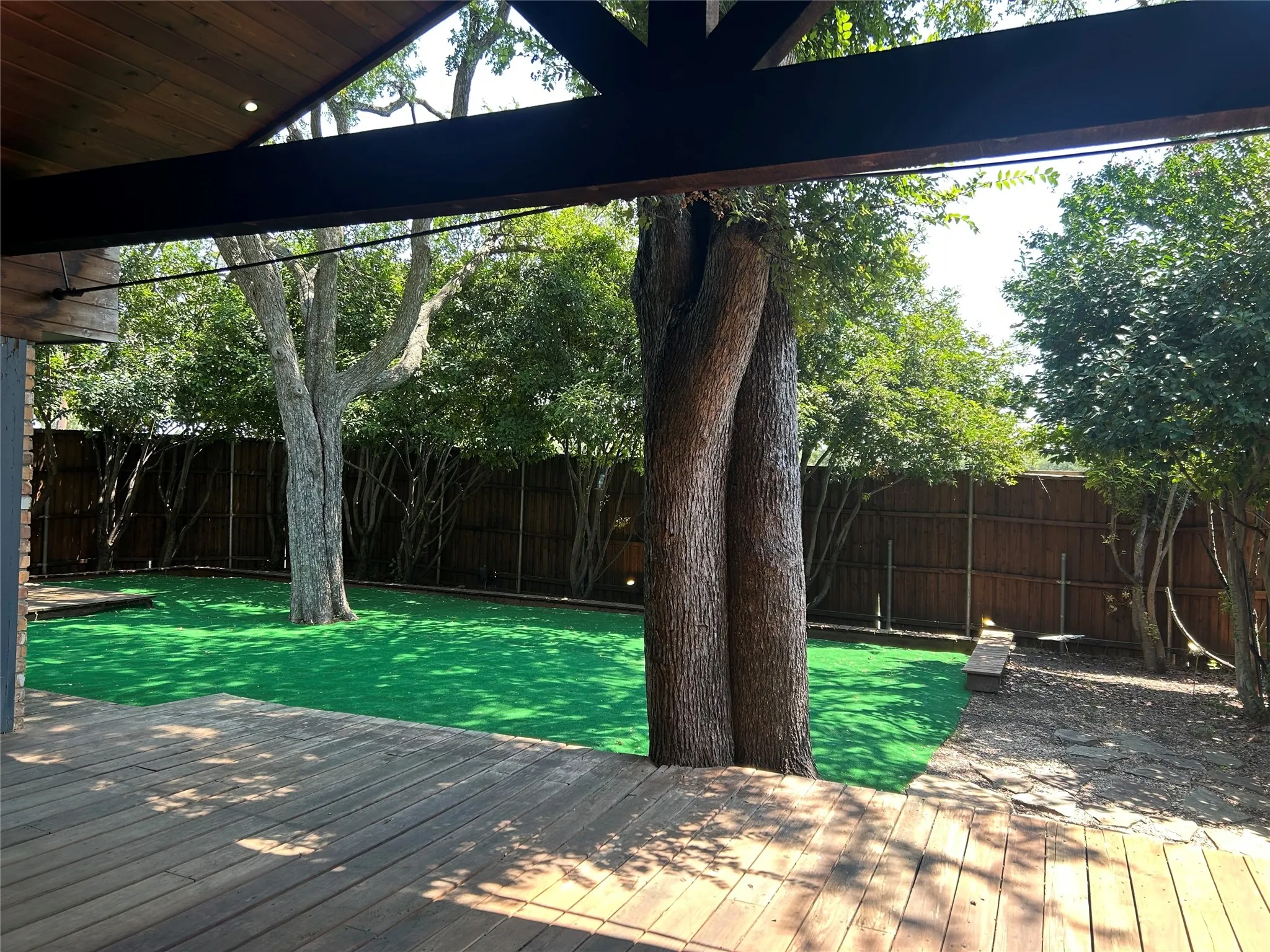 The wood deck with a covered patio overlooks a private yard with mature trees and shrubs.
