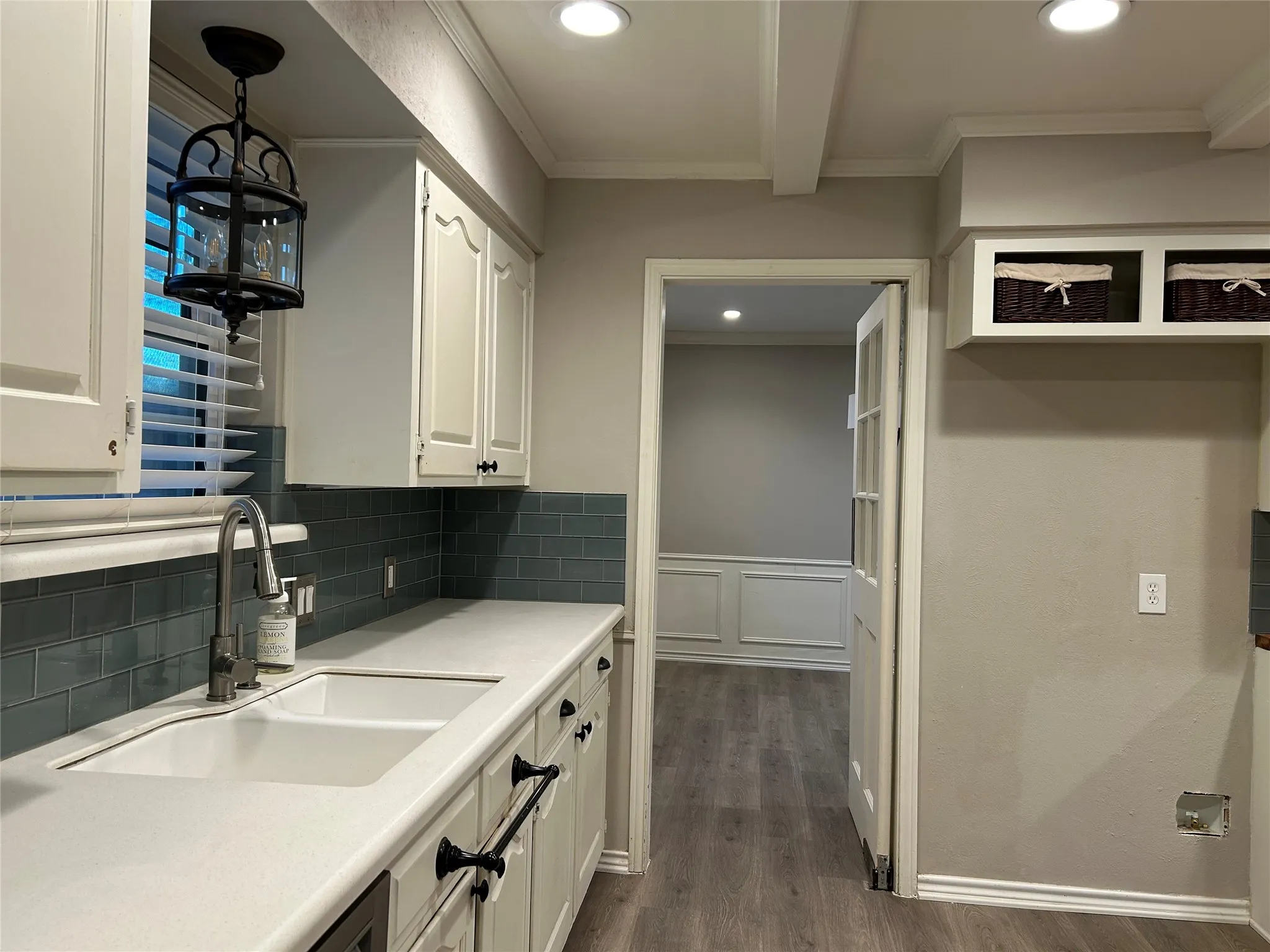 The kitchen features a double basin sink, white cabinetry with dark hardware, subway tile backsplash, and light-colored countertops.