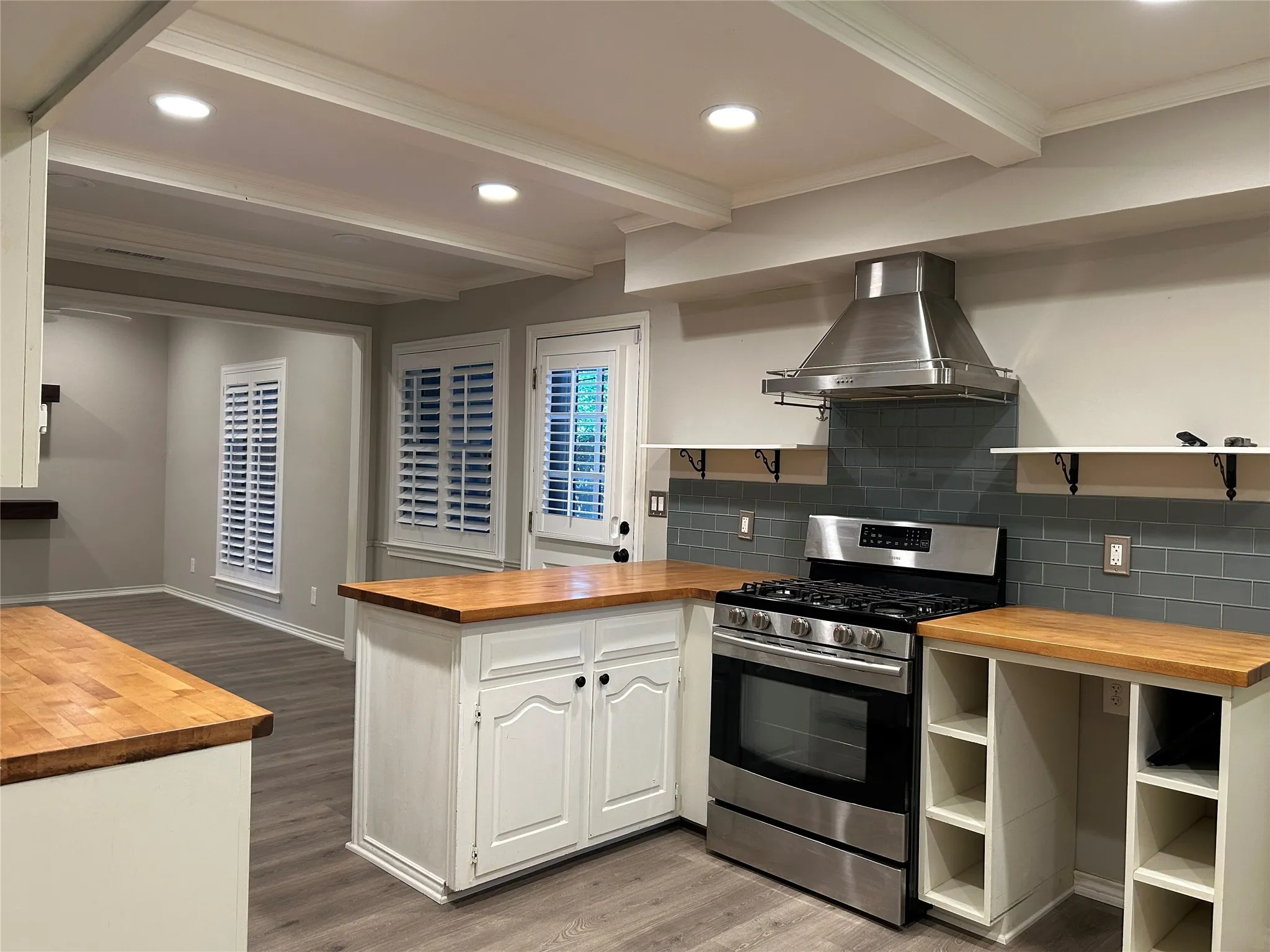 The kitchen opens to the family room and features butcher block countertops, subway tile backsplash, stainless steel gas range, and a matching stainless steel range hood.