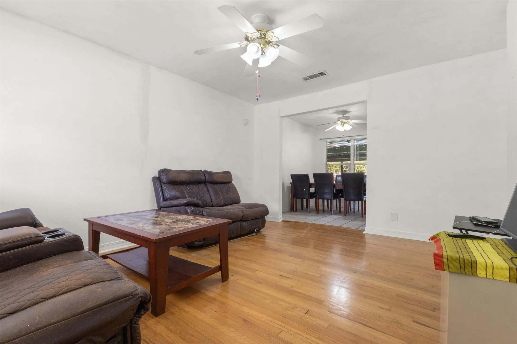 Wood-finish flooring throughout, ceiling fan with integrated lighting, and a wide cased opening to an additional room