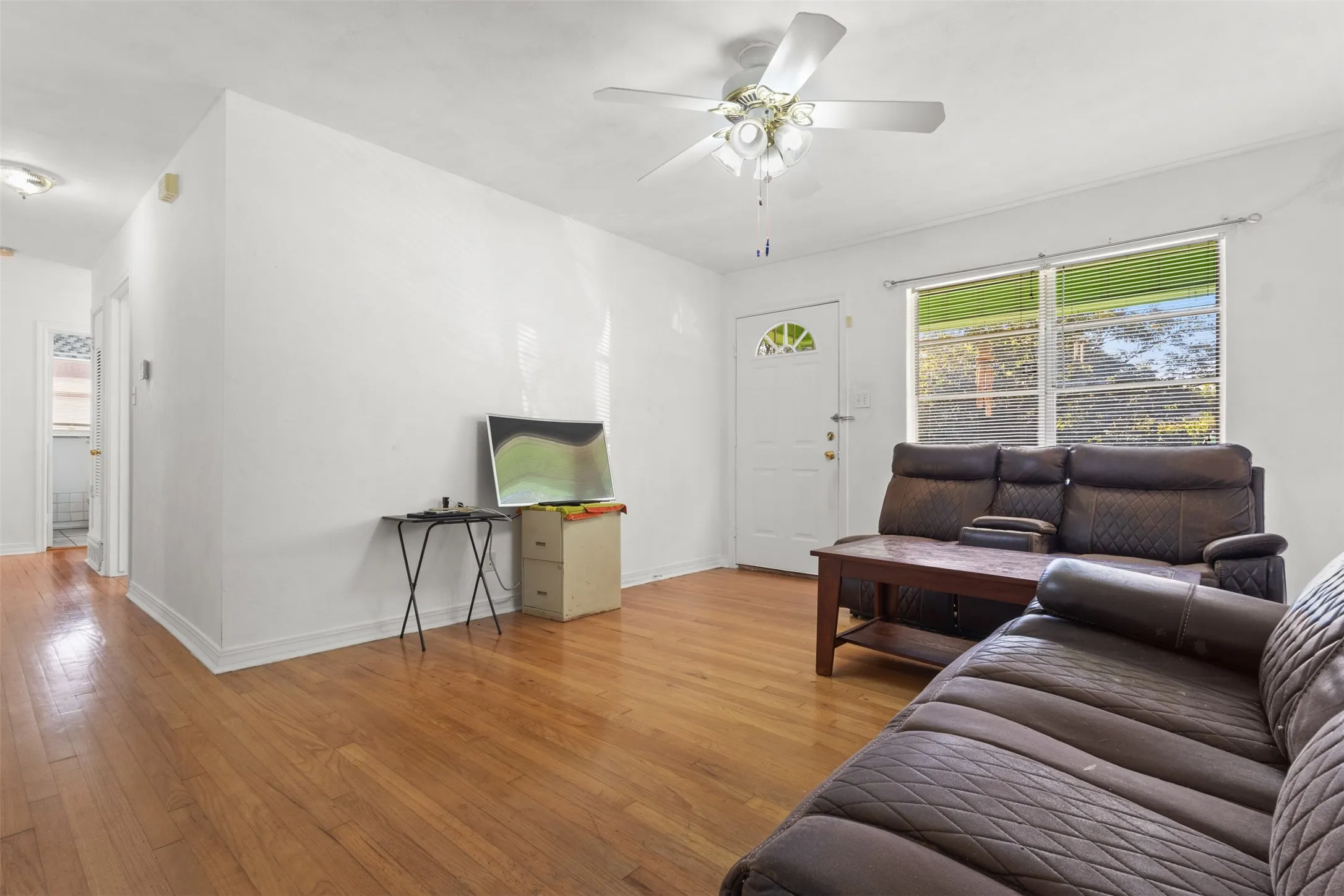 Wood-finish flooring, white walls, ceiling fan with light fixture, and a white entry door with a decorative window