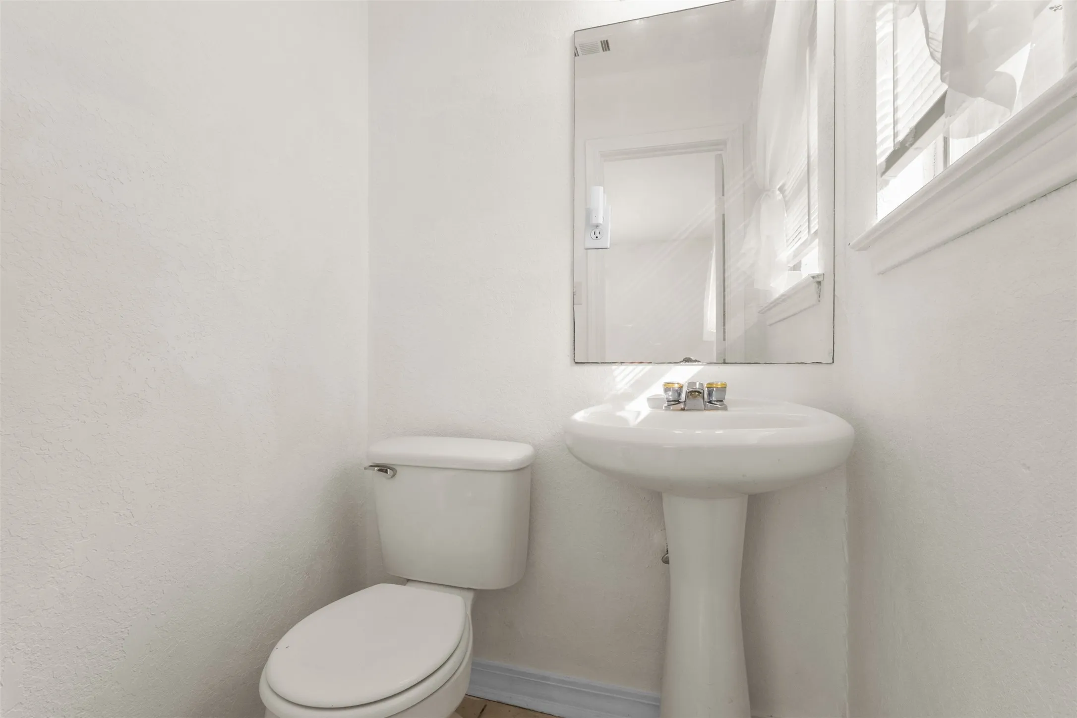 Pedestal sink with polished chrome faucet, rectangular wall mirror, and a white toilet
