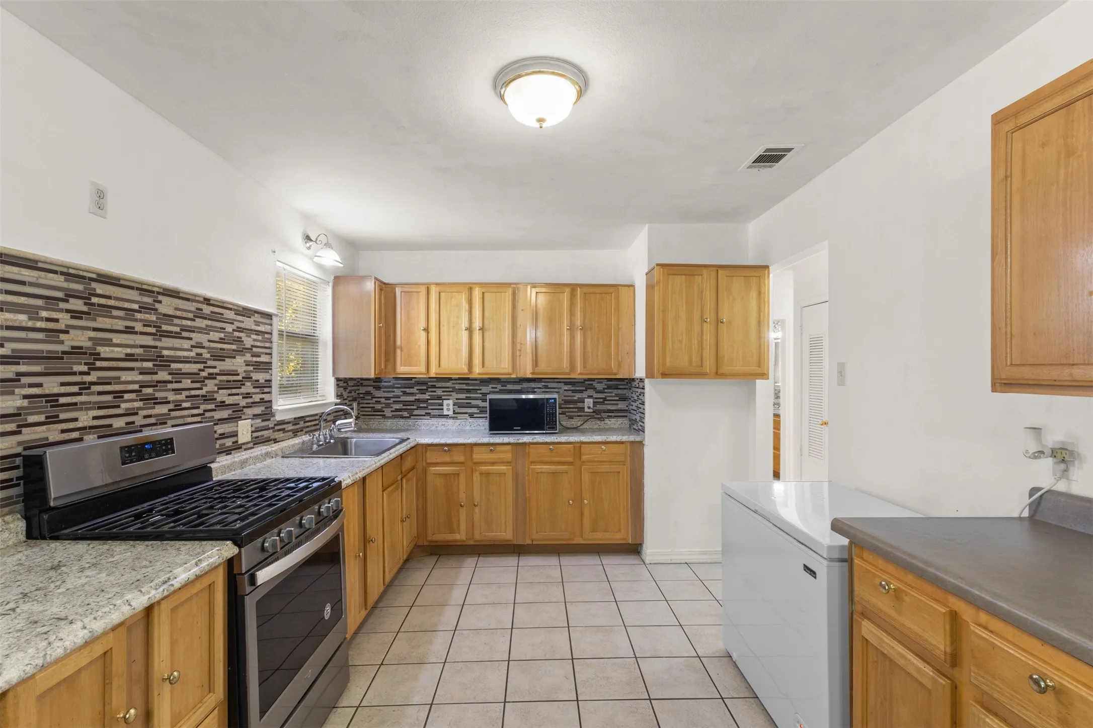 Kitchen featuring wood cabinetry, stainless steel range, light-toned countertops, tile flooring, and a mosaic tile backsplash