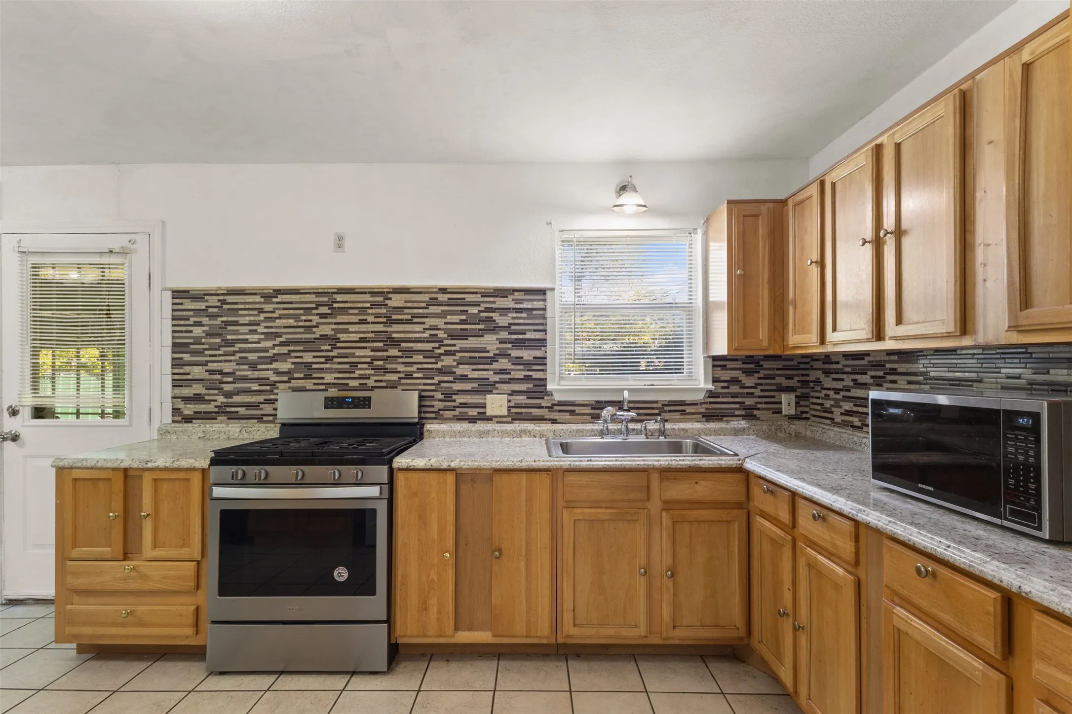 Wood-finish cabinetry paired with light-toned countertops and a mosaic tile backsplash