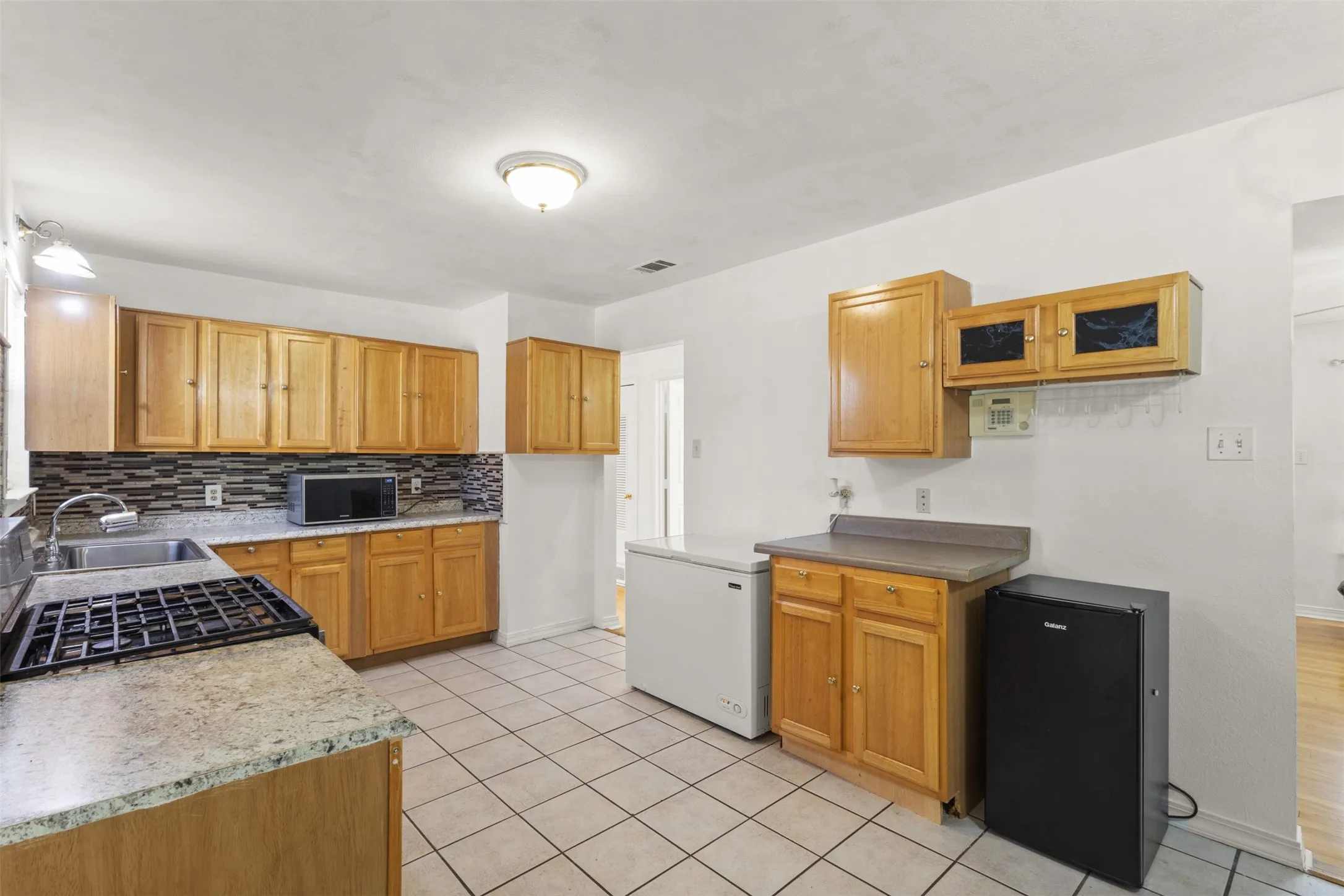 Kitchen featuring wood cabinetry, stone-finish countertops, a tile backsplash, and tile flooring