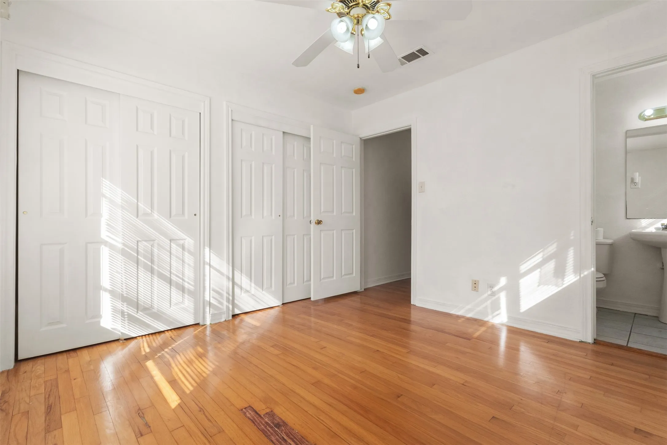 Hardwood flooring, ceiling fan with integrated lighting, two panel doors, an open doorway, and a lavatory with pedestal sink