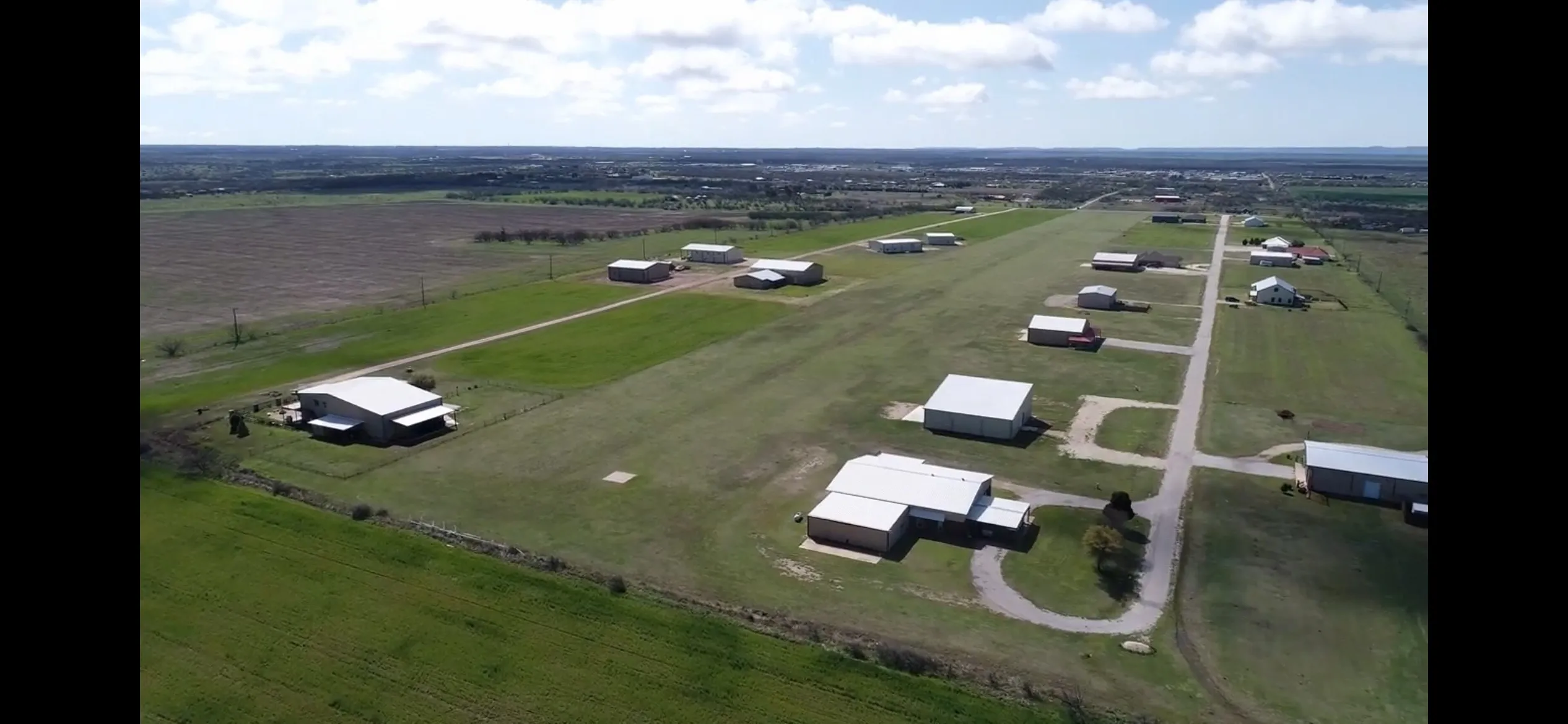 Expansive acreage featuring multiple structures, a paved runway, and clear sky overhead