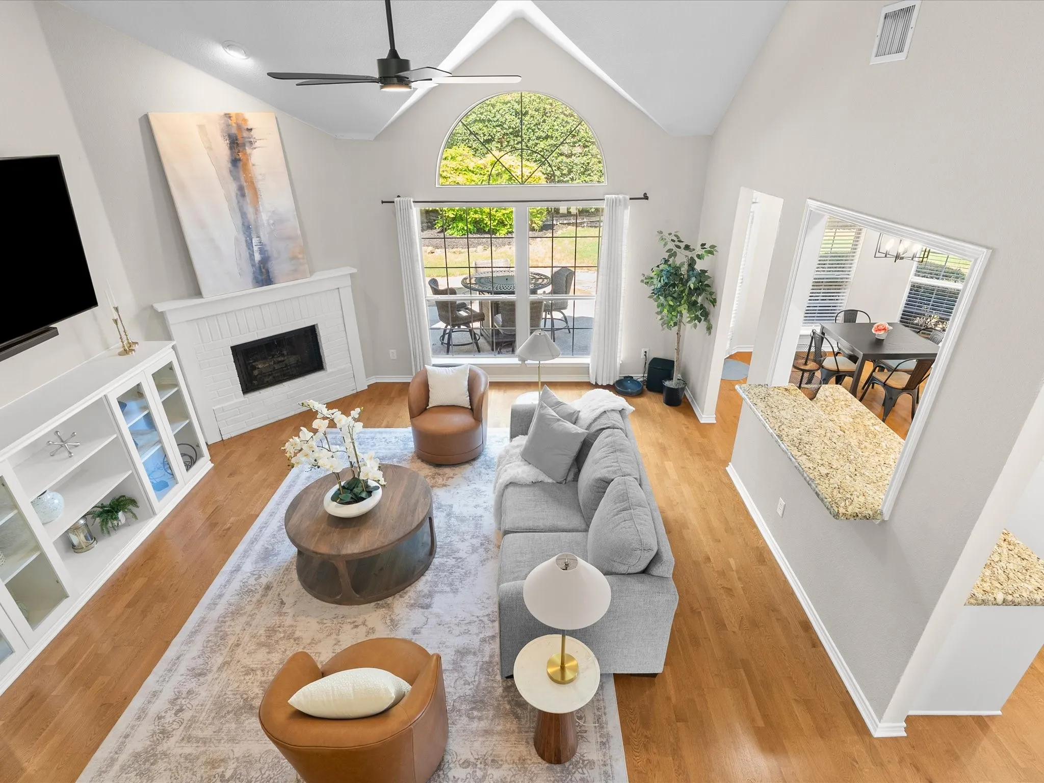 Vaulted ceiling, arched transom window, wood-finish flooring, white brick fireplace, built-in display cabinetry