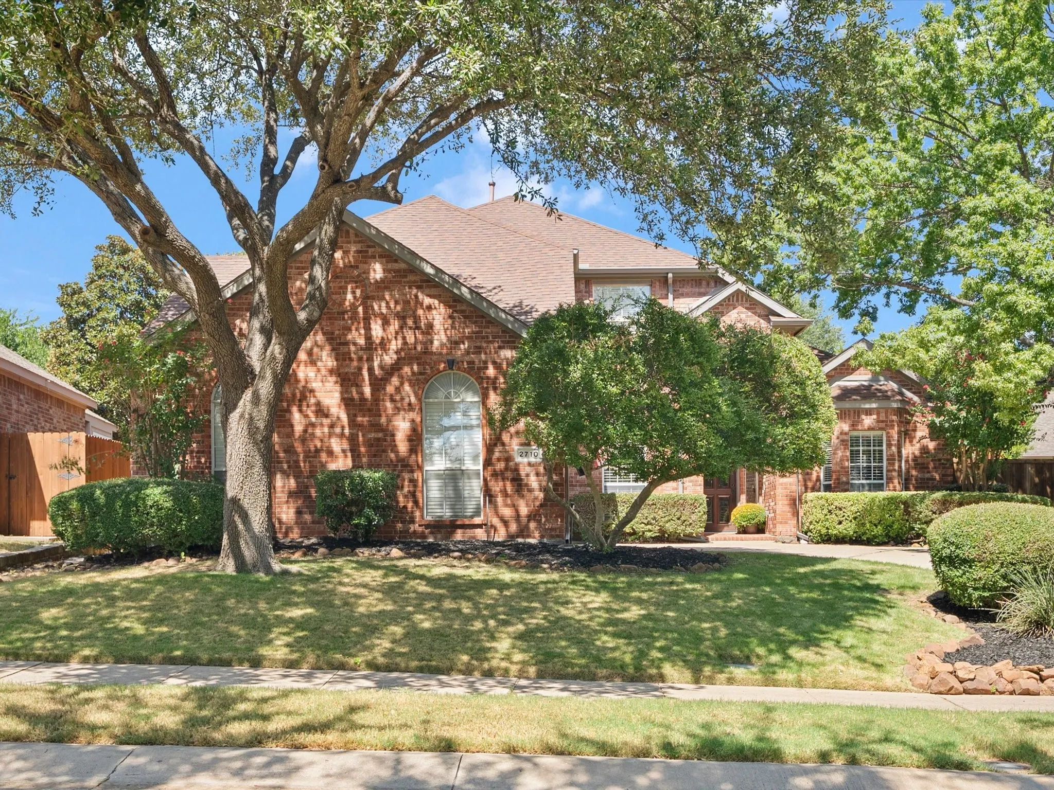 Traditional brick exterior featuring arched windows, a multi-gabled roofline, and established landscaping