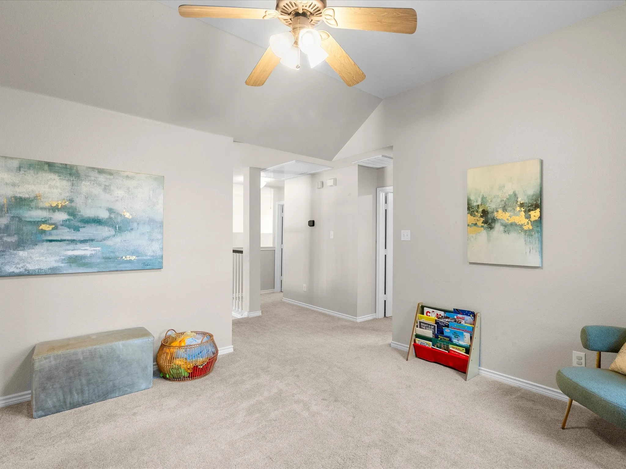 Vaulted ceiling with a ceiling fan, carpeted flooring, and a hallway featuring a metal spindle railing