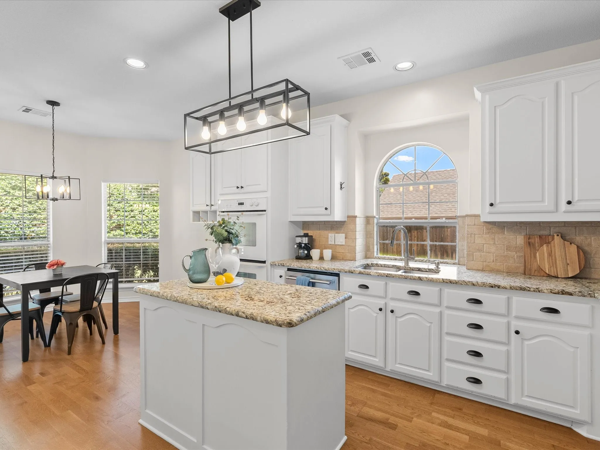Kitchen featuring wood-finish flooring, white cabinetry, granite countertops, and a center island