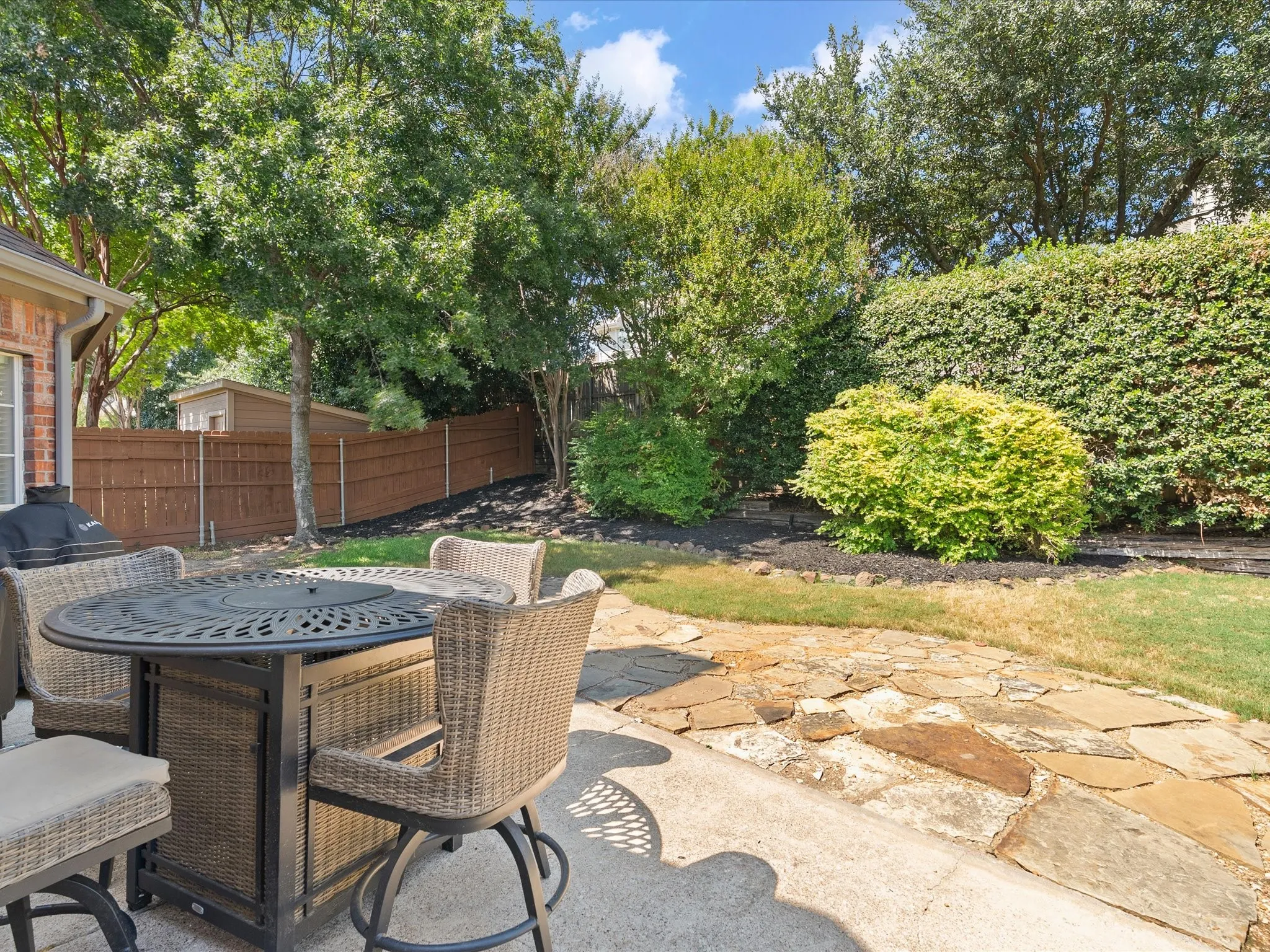 Patio featuring concrete and flagstone surfacing, bordered by manicured landscaping, a wood fence, and mature trees