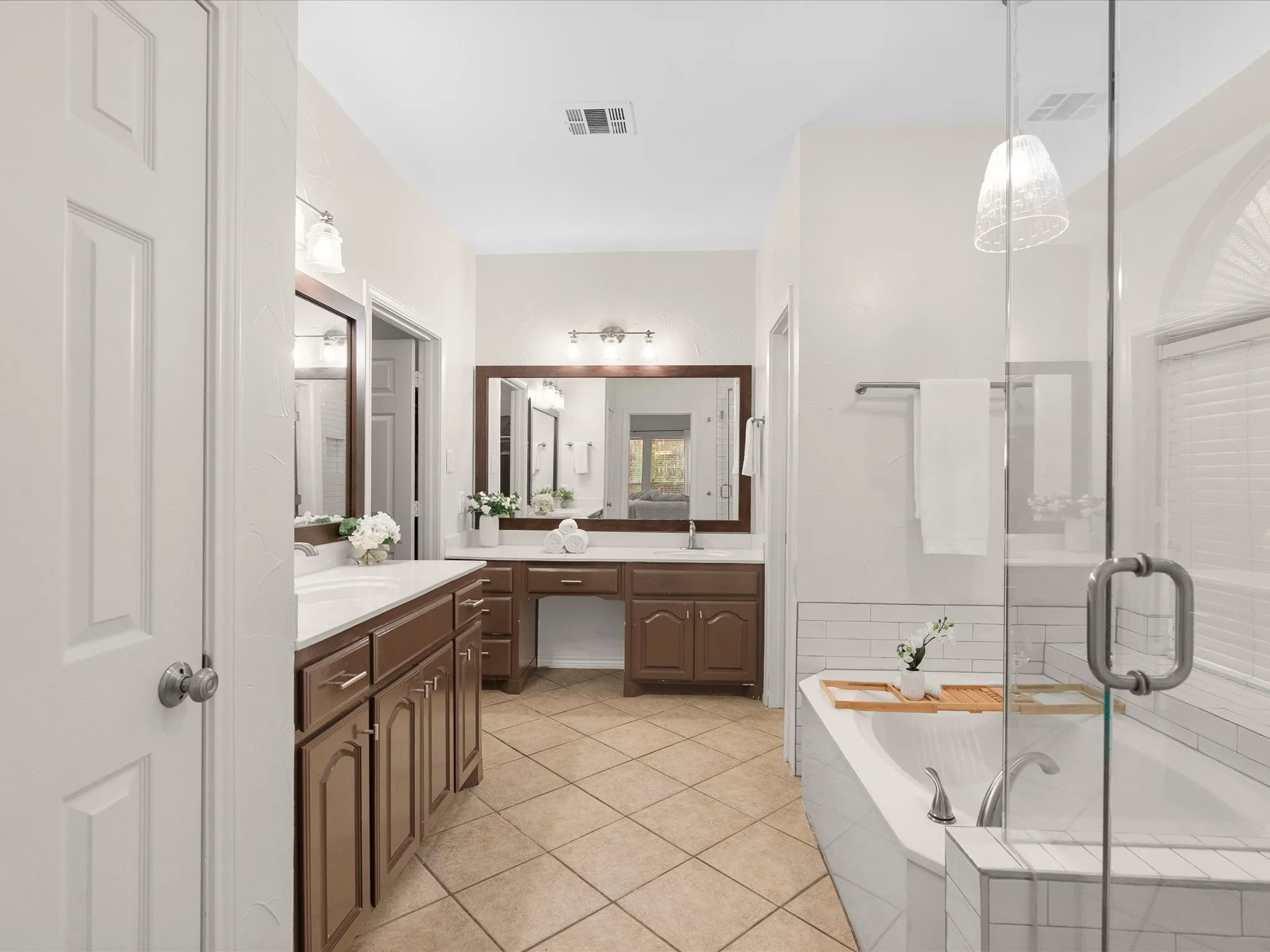 Dual vanity with wood-finish cabinetry, built-in vanity area, tile flooring, corner soaking tub with subway tile surround, and glass-enclosed shower