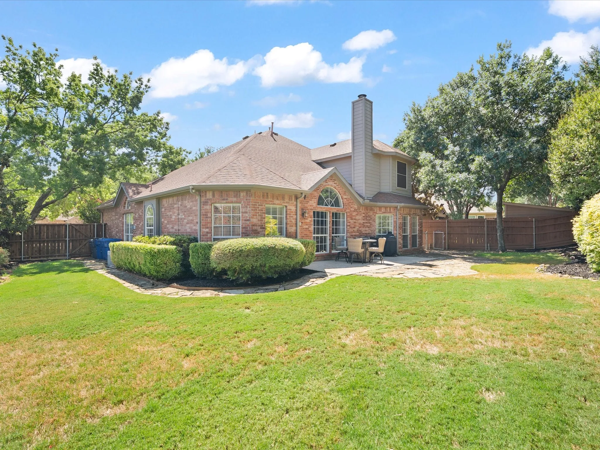 Brick exterior with a stone patio, mature trees, and a private fenced yard