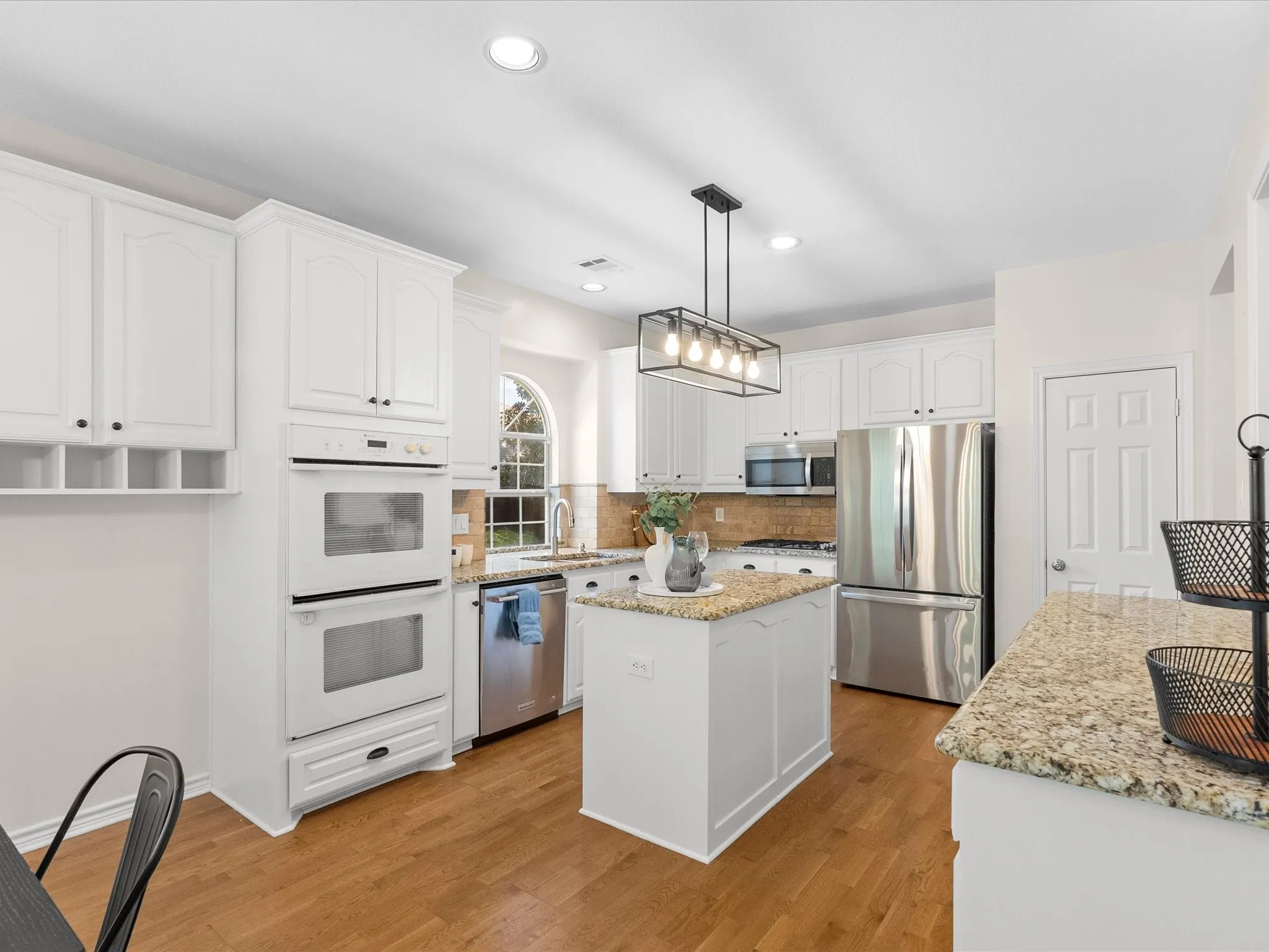 White cabinetry, granite countertops, stainless steel appliances, wood-finish flooring, and a contemporary linear pendant light fixture