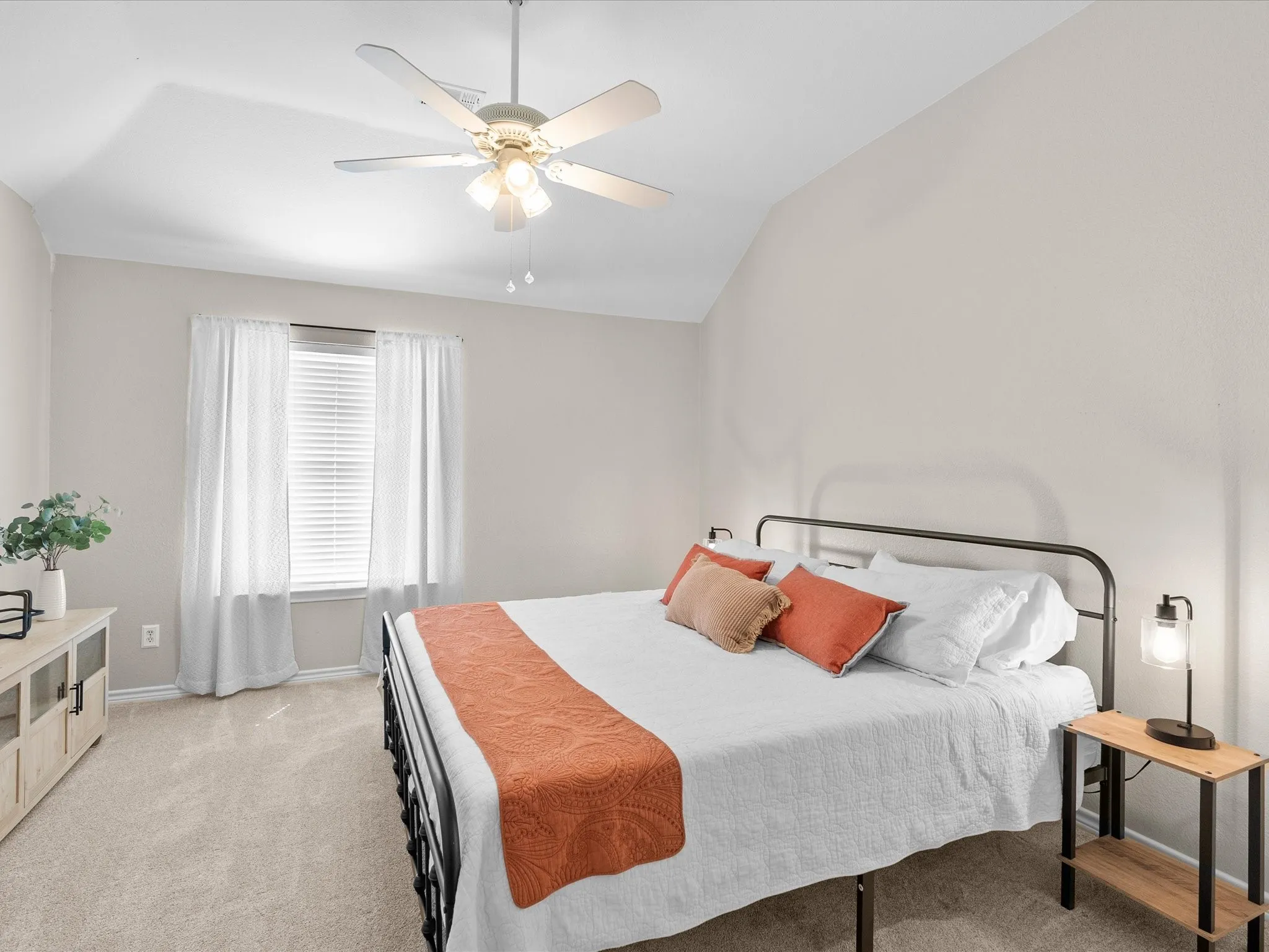 Vaulted ceiling, ceiling fan with integrated lighting, window with blinds and sheer curtains, and neutral-toned wall paint