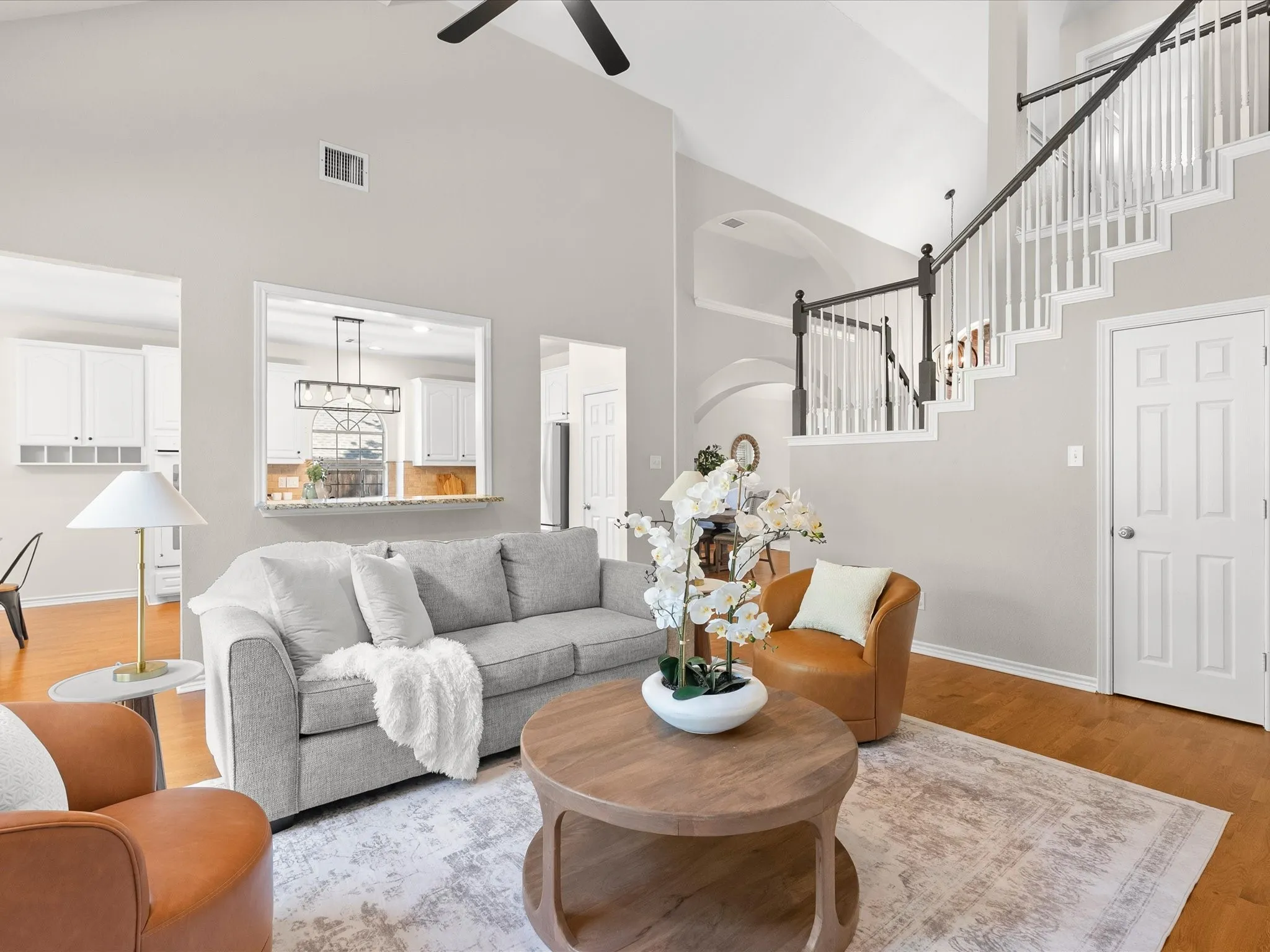 Vaulted ceiling, wood-finish flooring, staircase with white balusters and dark handrail, pass-through window with granite countertop, recessed lighting