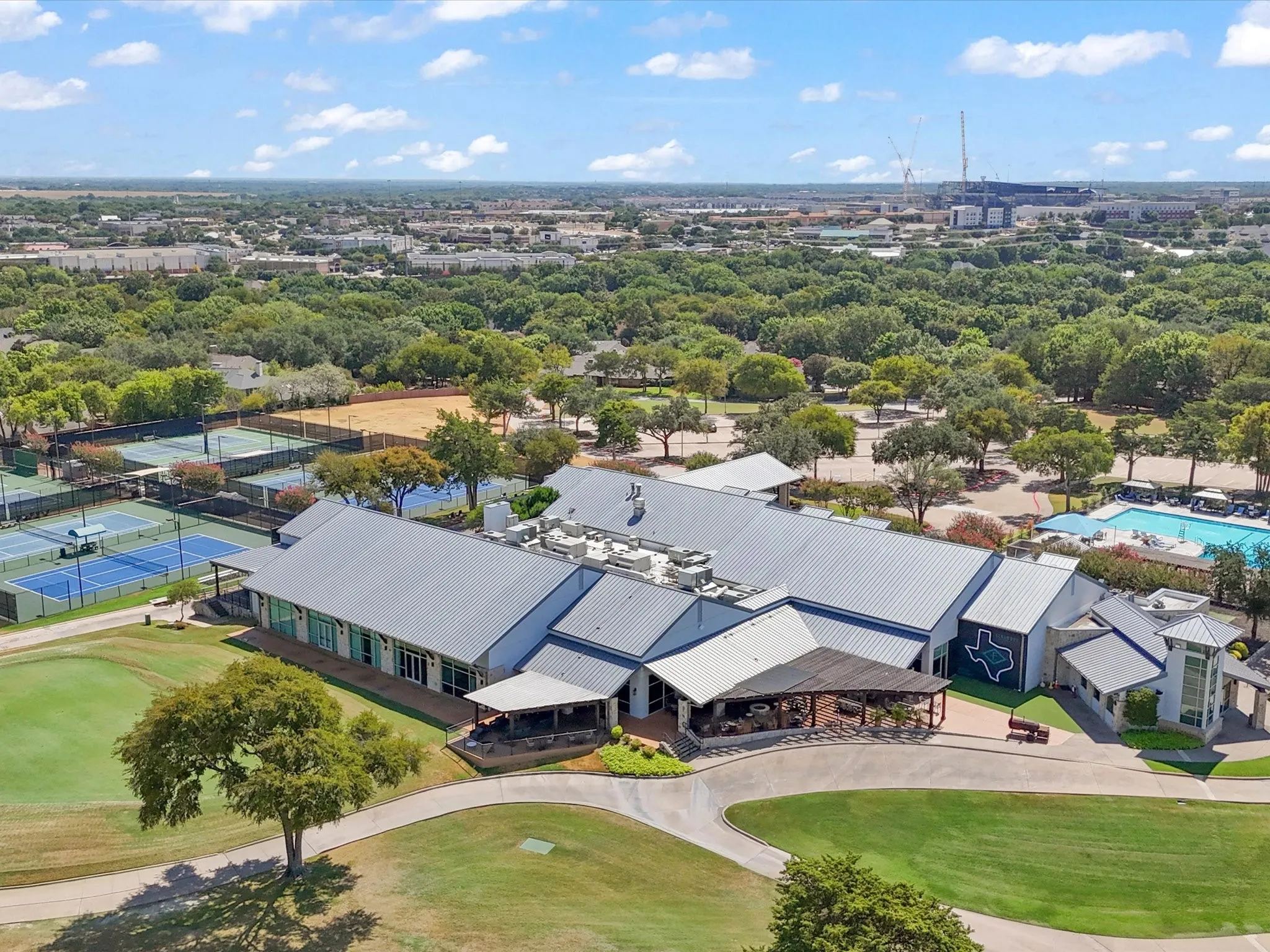 Expansive property featuring a large building with a metal roof, multiple tennis courts, a swimming pool, and a golf course