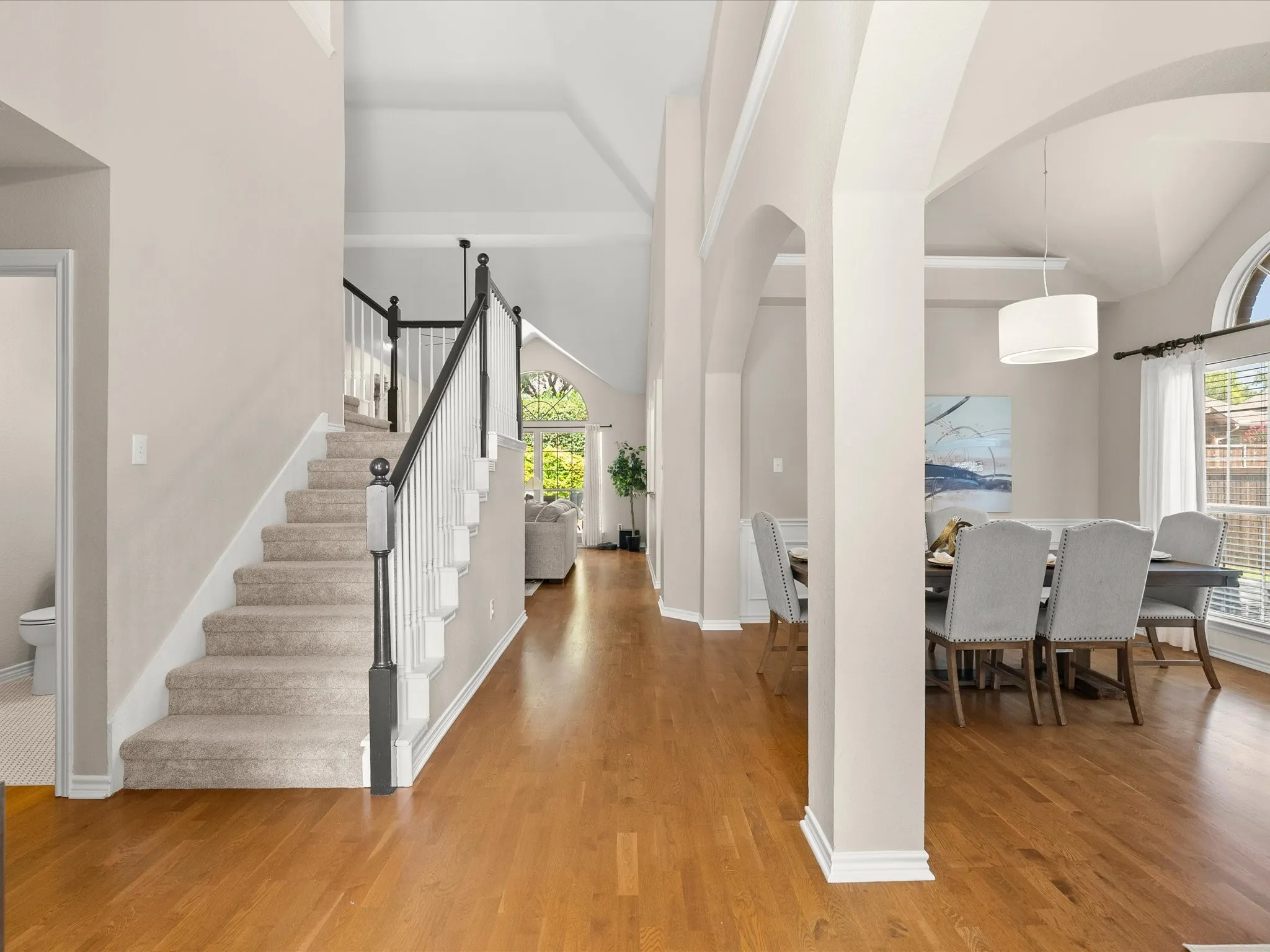 Wood-finish flooring, vaulted ceilings, arched doorways, a carpeted staircase with a wood handrail, and a drum pendant light fixture