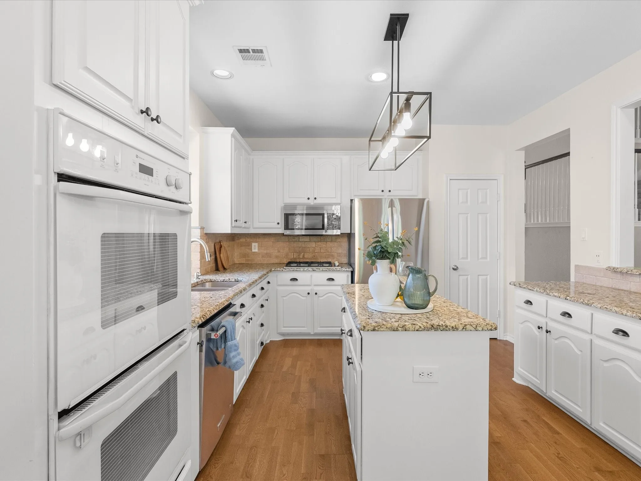 Kitchen featuring white cabinetry, built-in double ovens, light granite countertops, a center island, and wood-finish flooring